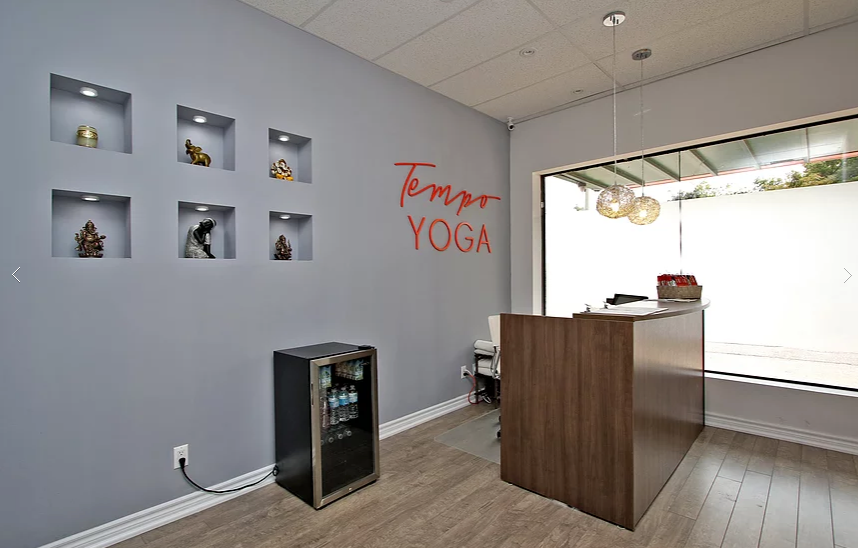 This Richmond Hill yoga studio interior renovation showcases a clean and welcoming reception area designed and built by Reno Compass. The space features a modern wood reception desk, soft grey feature walls, custom recessed display niches with accent lighting, and branded wall signage that enhances the studio’s identity. Large front windows allow natural light to brighten the space, creating a calm and professional atmosphere for clients. As a trusted Toronto renovation company, Reno Compass delivers stylish and functional commercial interiors tailored for yoga studios, wellness centers, and retail businesses seeking a refined customer experience.