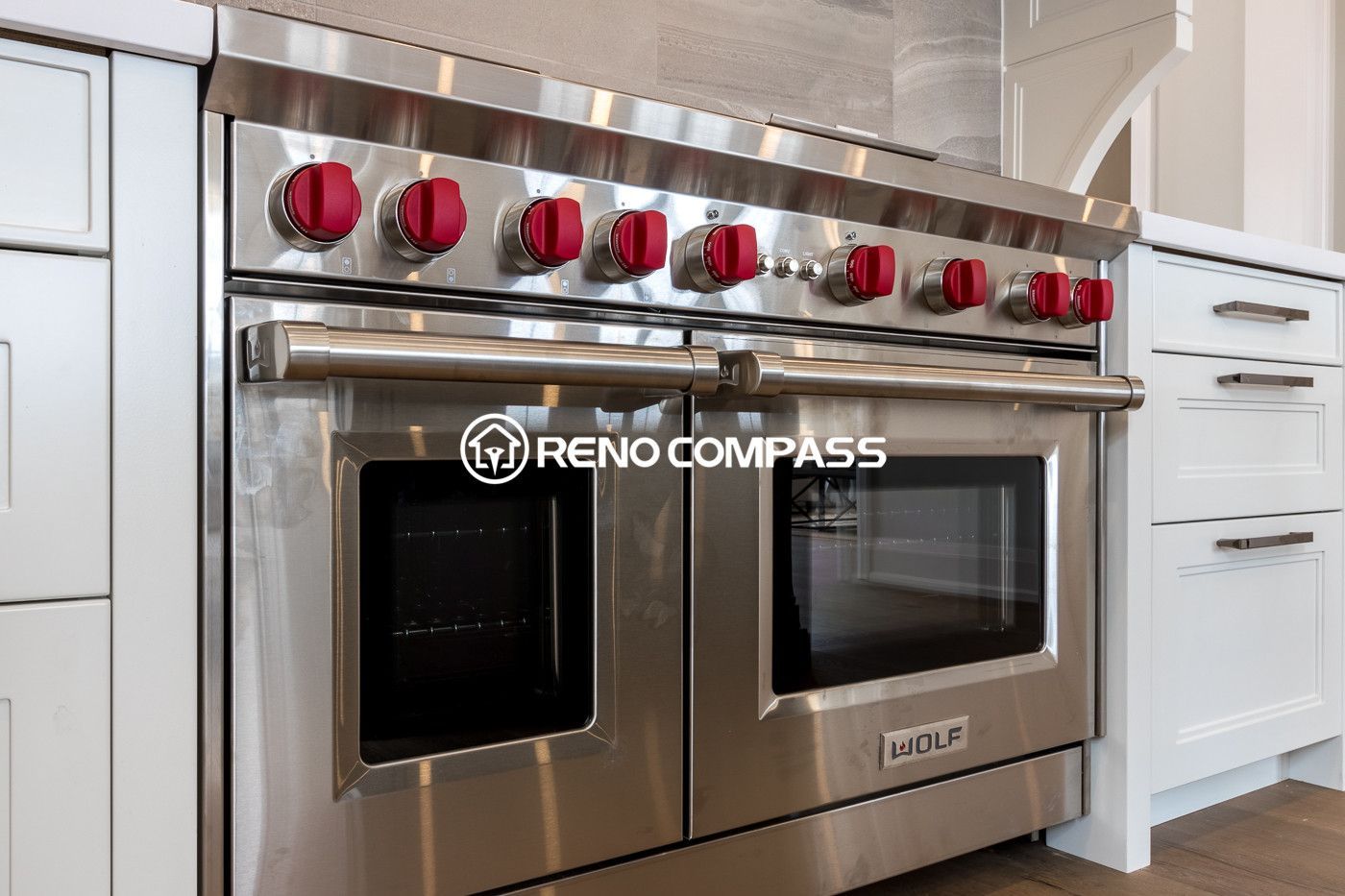 High-end kitchen renovation in Newmarket featuring a Wolf professional gas range with signature red knobs, custom white cabinetry, and modern engineered hardwood flooring. This luxury appliance installation highlights the premium design and functionality of the renovated kitchen space.