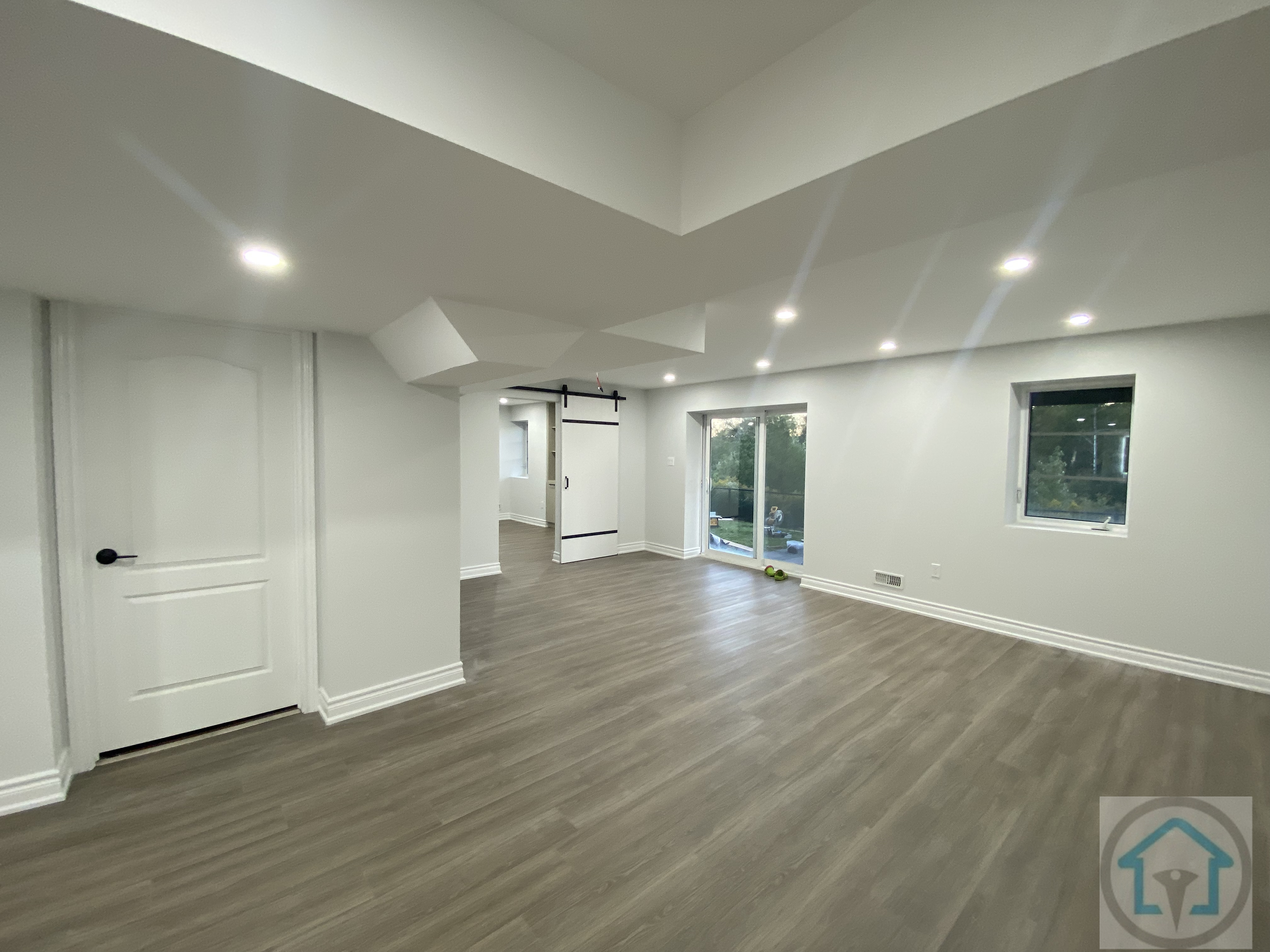 This Aurora basement renovation features an open-concept layout with modern flooring, bright recessed lighting, and clean white walls. The design maximizes natural light and creates a versatile living space suitable for family activities or entertainment. Contractor: Reno Compass Inc., City: Aurora.