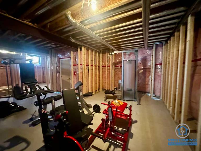 Unfinished basement in Newmarket before renovation, showing exposed framing, insulation, and temporary gym equipment. Raw space before full transformation.