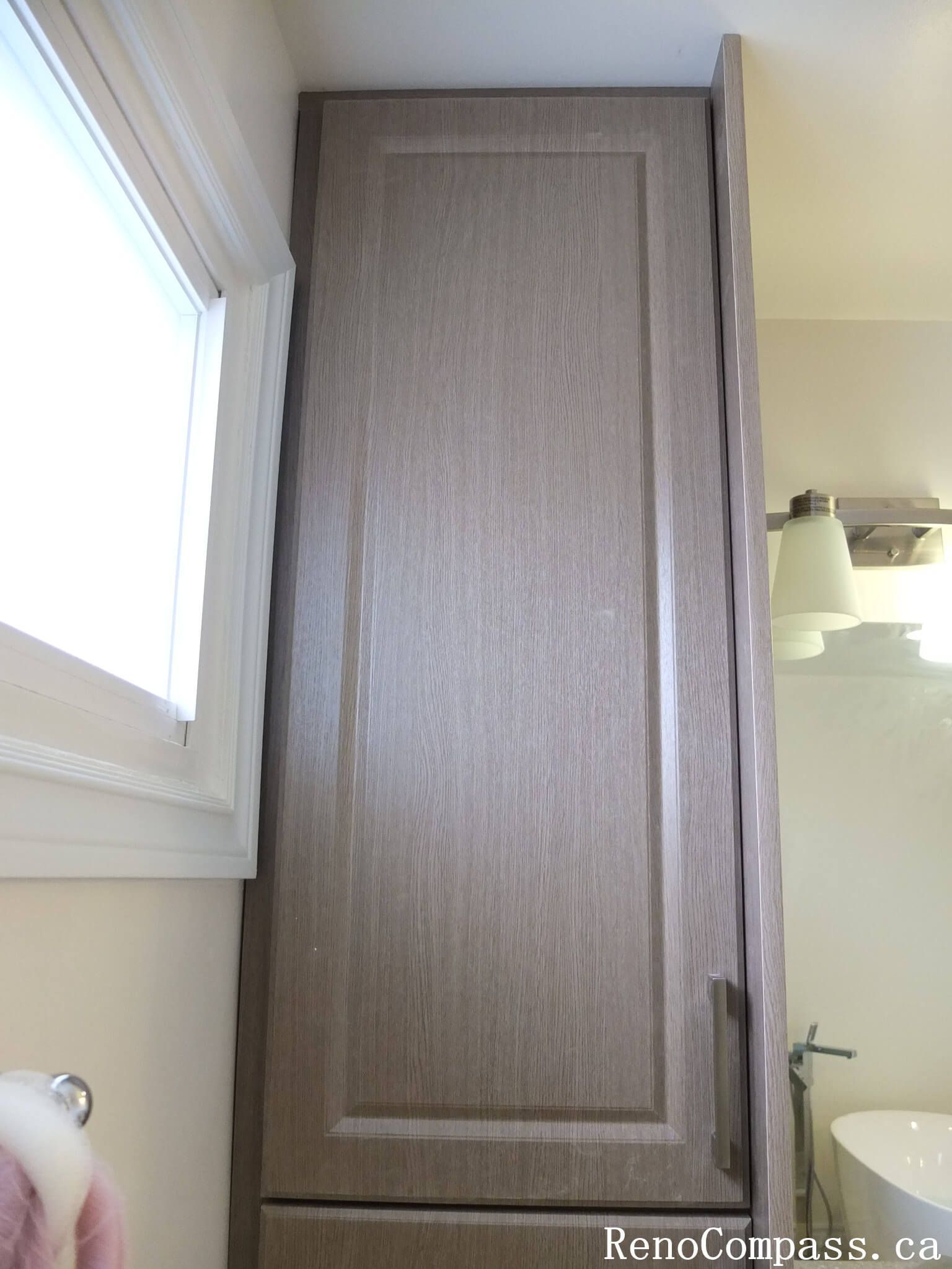 Bathroom renovation in North York featuring a floor-to-ceiling tall storage cabinet with wood-grain finish, maximizing vertical space beside the vanity area. This Toronto interior renovation emphasizes efficient storage planning, clean lines, and seamless integration with modern bathroom layouts.