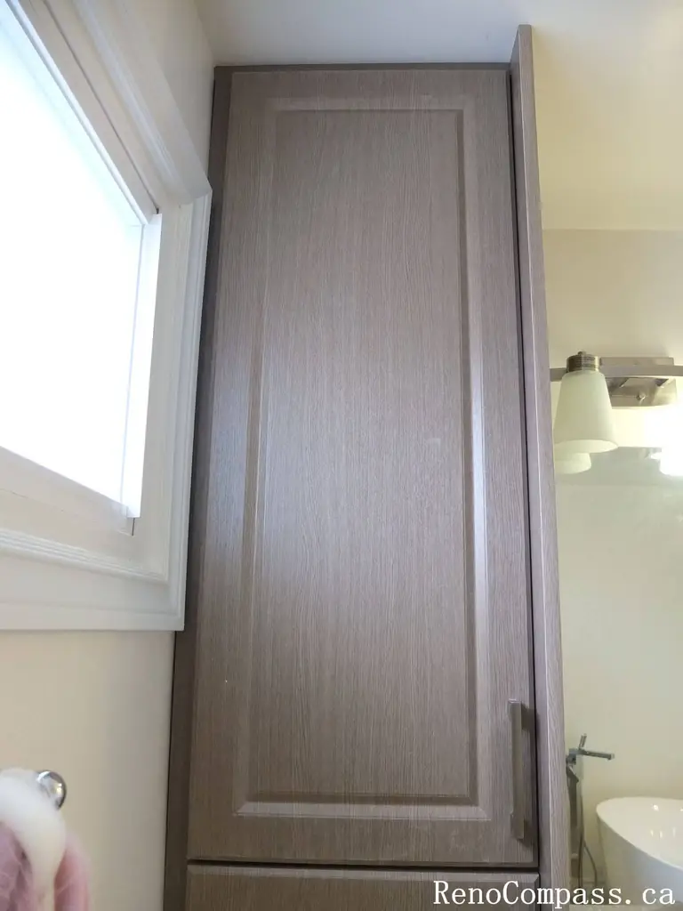 Bathroom renovation in North York featuring a floor-to-ceiling tall storage cabinet with wood-grain finish, maximizing vertical space beside the vanity area. This Toronto interior renovation emphasizes efficient storage planning, clean lines, and seamless integration with modern bathroom layouts.