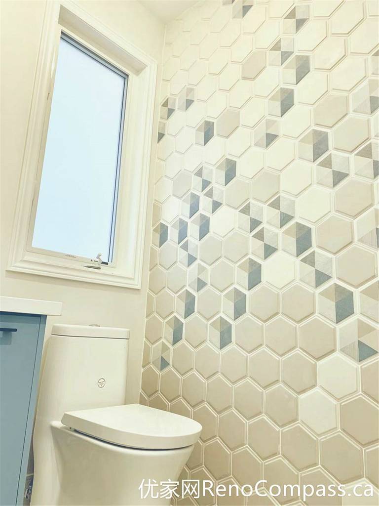 This Markham home renovation highlights a stylish bathroom featuring a soft blue vanity, round mirror, and a decorative hexagon tile accent wall. The combination of warm lighting, modern fixtures, and natural daylight from the window creates a cozy yet contemporary atmosphere with strong visual character.