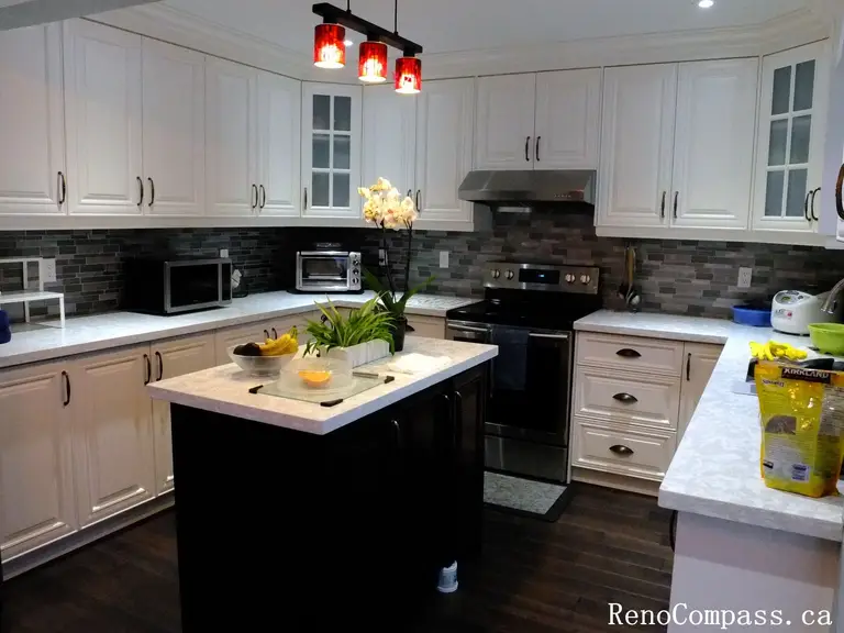 This Richmond Hill kitchen renovation showcases a modern white cabinet design with a central island, quartz countertops, and stainless steel appliances. The space is enhanced by stylish pendant lighting and a sleek backsplash, creating a clean and functional cooking environment. Completed by a Toronto renovation company, this project highlights contemporary kitchen design with practical layout and elegant finishes.