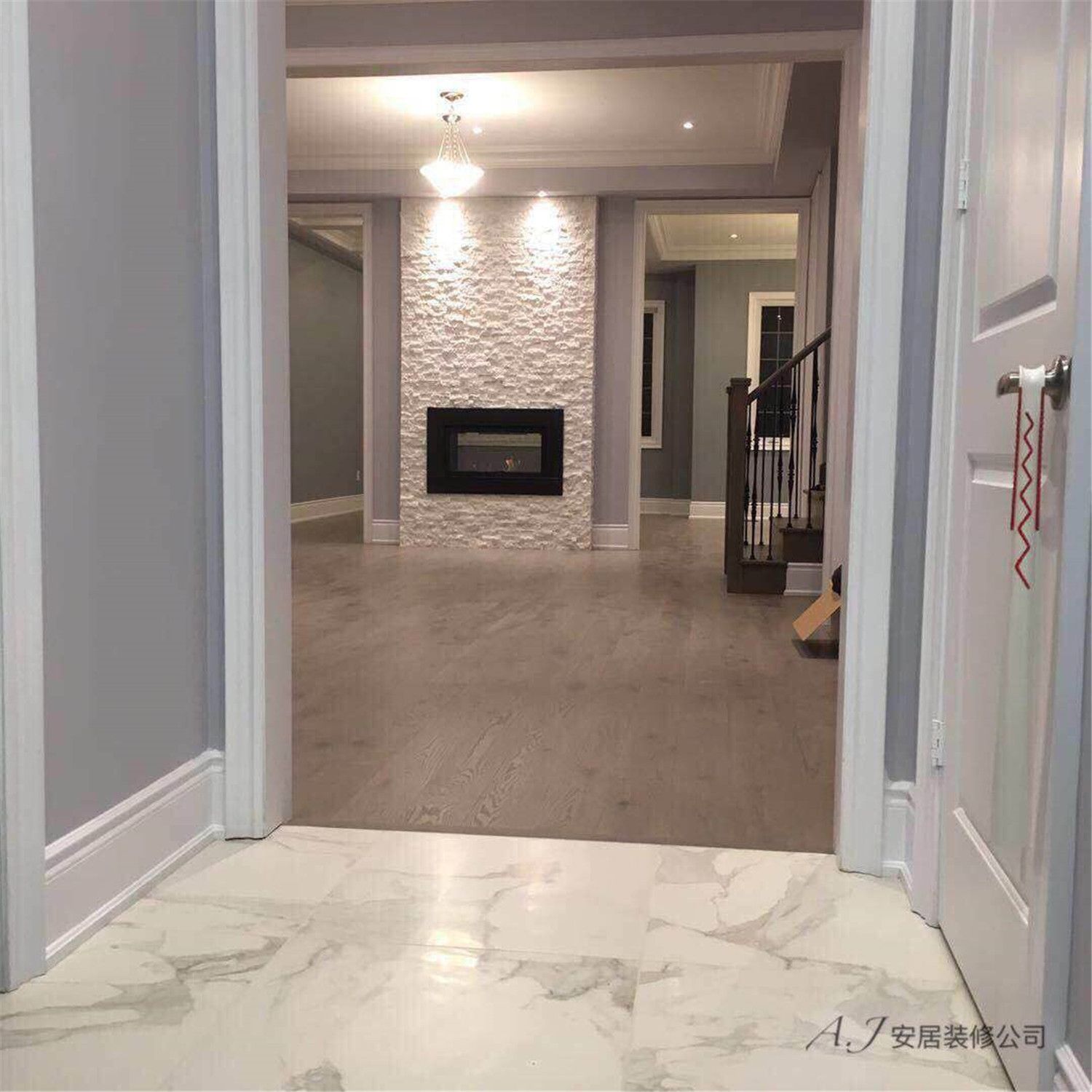 This Scarborough interior renovation highlights a welcoming entrance view leading into a modern living space. The design features marble-look floor tiles at the entry, warm wood flooring throughout the main area, and a textured stone fireplace feature wall as the focal point. Recessed lighting, neutral grey walls, and elegant trim details create a clean and contemporary interior layout, enhancing both visual depth and everyday functionality for this Scarborough home.