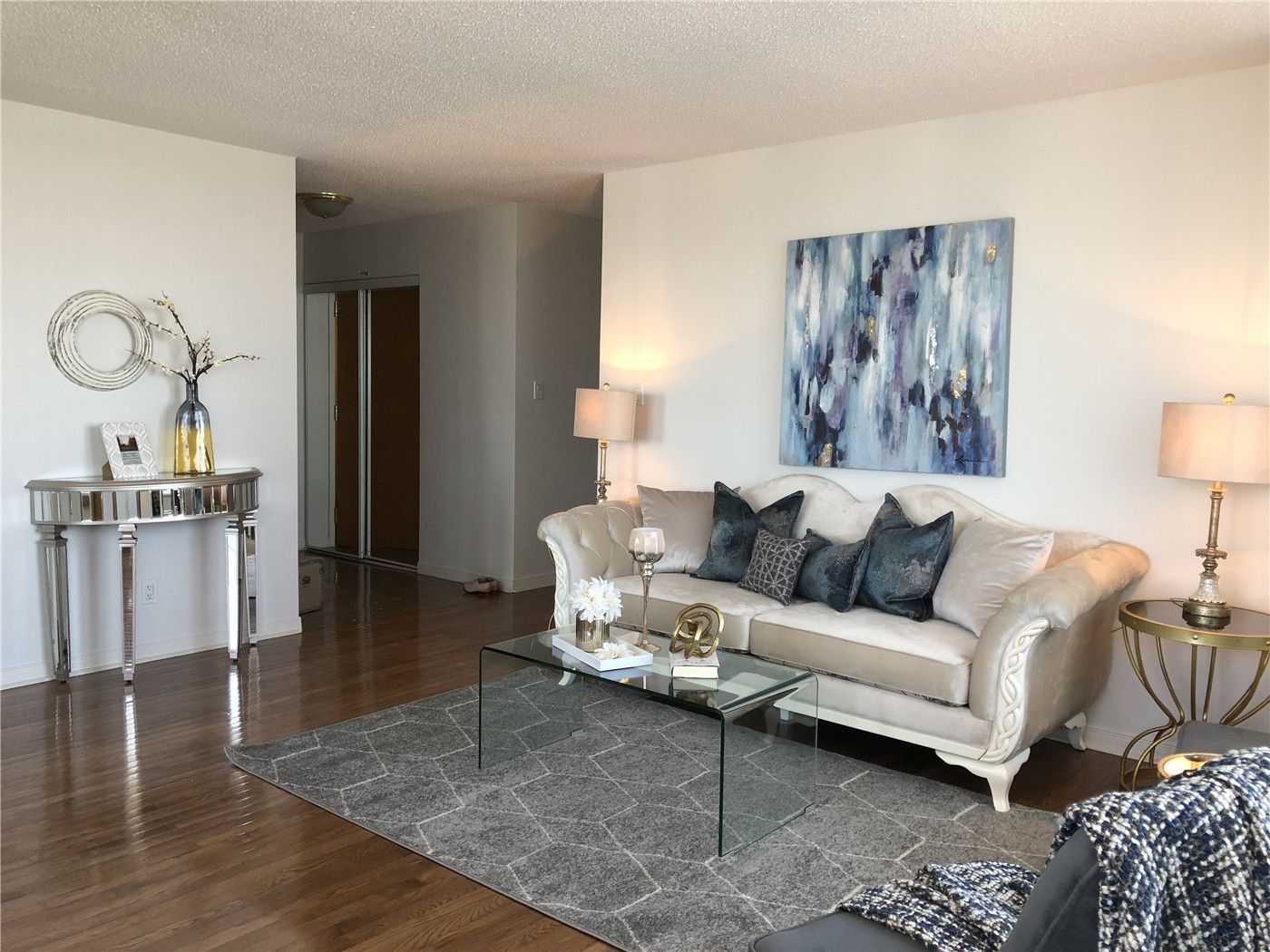 This Toronto interior design pre-sale staging features a bright and modern living room with polished hardwood flooring, a neutral-tone sofa, glass coffee table, and contemporary artwork. Thoughtful furniture placement and coordinated décor create a spacious, elegant atmosphere that enhances natural light and flow.