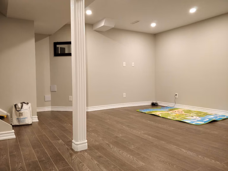 This Scarborough basement renovation features a spacious finished area with modern pot lighting, fresh painted walls, and high-quality hardwood flooring. A structural support column is seamlessly integrated into the layout while maintaining an open and functional design. The renovation transforms the basement into a bright and practical living space, completed by a professional Toronto renovation company.