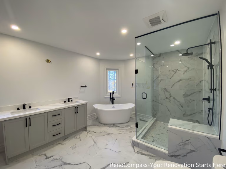 This Thornhill master bathroom renovation presents a bright, open layout featuring a double sink vanity, a freestanding bathtub, and a frameless glass walk-in shower. Marble-look porcelain tiles unify the floor and shower walls, creating a seamless and elegant visual flow throughout the space. Matte black fixtures add modern contrast, while recessed lighting and natural daylight enhance brightness and spatial balance. The thoughtful layout improves functionality, comfort, and long-term usability, delivering a refined and timeless bathroom design.