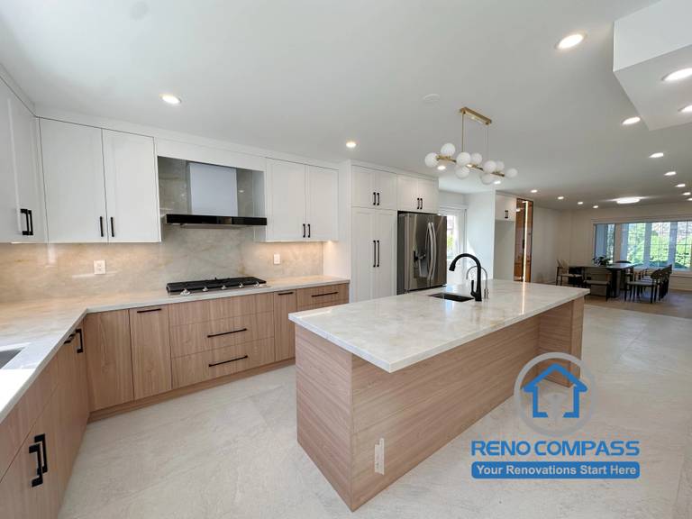 A luxury open-concept kitchen featuring a large quartz waterfall island, custom two-tone cabinetry, premium stainless steel appliances, and integrated under-cabinet lighting. Completed as part of a whole home renovation in Markham, Ontario, this contemporary kitchen combines elegant design, functional storage, and seamless indoor living with expert craftsmanship by Reno Compass.