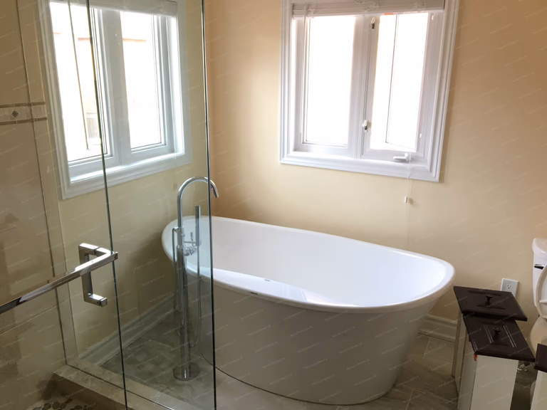 This Markham interior renovation showcases a spa-inspired bathroom featuring a modern freestanding bathtub, frameless glass shower enclosure, and elegant tile flooring. Large windows bring in natural light, creating a bright and relaxing bathing space with a clean contemporary style. Completed by Reno Compass, a trusted Toronto renovation company specializing in bathroom and interior home renovations.