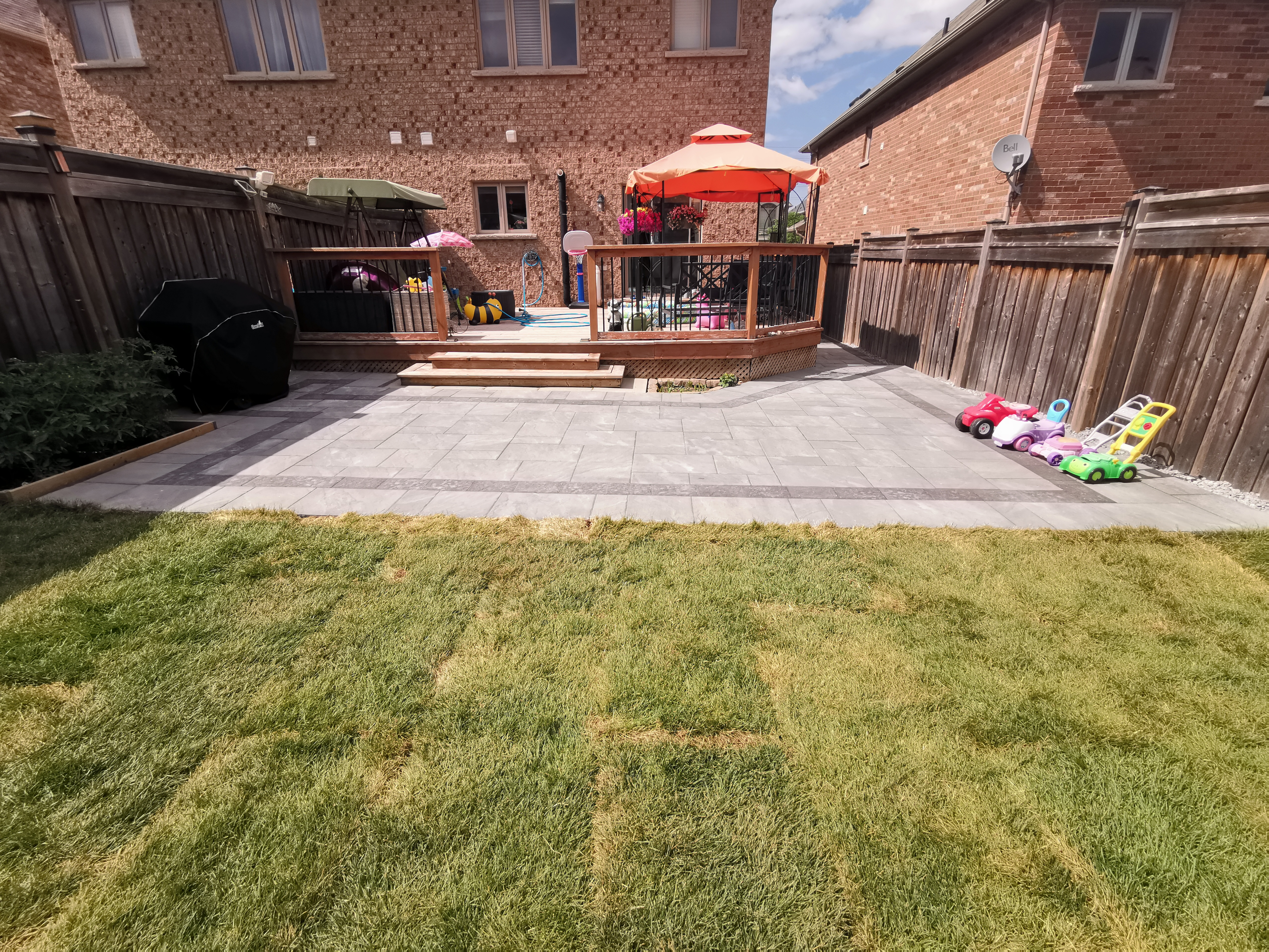 This Aurora backyard renovation showcases a full outdoor layout combining an interlocking paver patio, raised wooden deck, and open lawn area. The large-format concrete pavers create a clean, durable surface that enhances usability and visual balance, while the surrounding lawn provides a soft contrast for family-friendly outdoor activities. The patio connects seamlessly to the deck, forming a versatile outdoor living space suitable for relaxation, gatherings, and everyday use. This professionally completed interlocking project delivers a well-balanced, low-maintenance backyard solution for residential properties in Aurora.