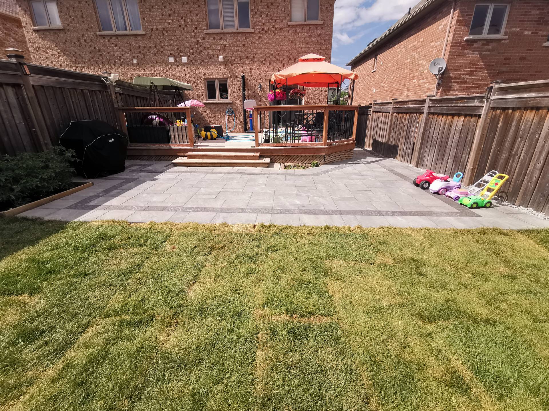 This Aurora backyard renovation showcases a full outdoor layout combining an interlocking paver patio, raised wooden deck, and open lawn area. The large-format concrete pavers create a clean, durable surface that enhances usability and visual balance, while the surrounding lawn provides a soft contrast for family-friendly outdoor activities. The patio connects seamlessly to the deck, forming a versatile outdoor living space suitable for relaxation, gatherings, and everyday use. This professionally completed interlocking project delivers a well-balanced, low-maintenance backyard solution for residential properties in Aurora.