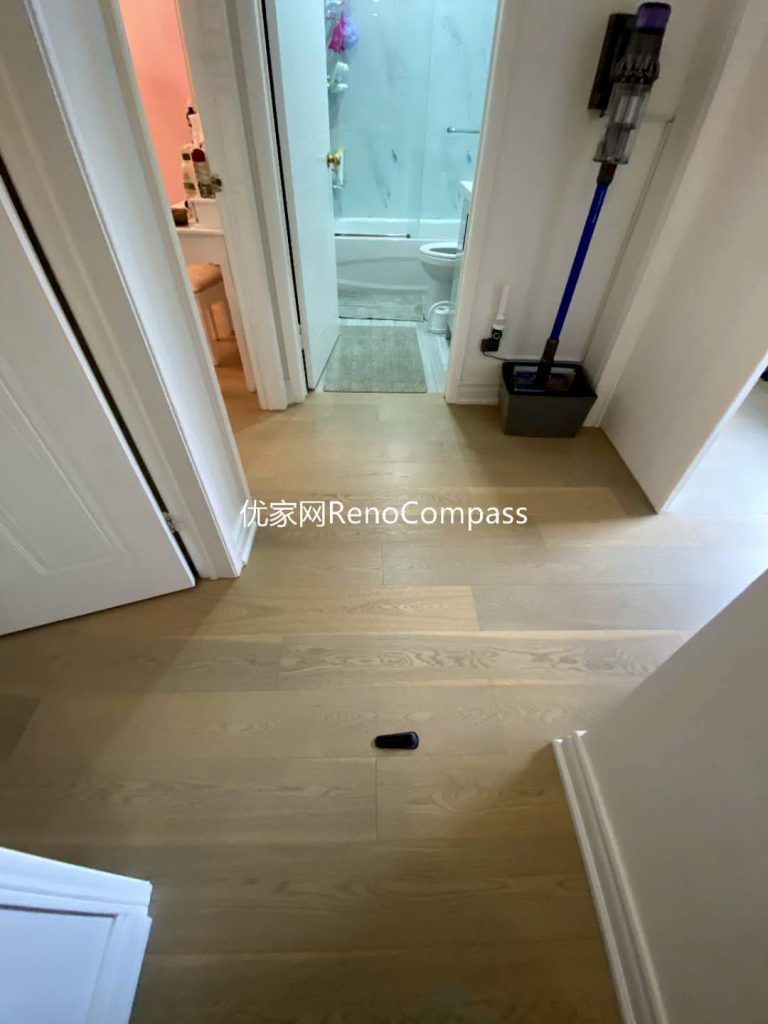 This image captures a finished interior renovation in Mississauga, focusing on the hallway flooring and its seamless transition into the bathroom area. Light-toned engineered wood flooring extends throughout the corridor, creating visual continuity and a clean, modern feel, while the bathroom features durable tile flooring designed for moisture resistance and safety. Precise floor alignment, clean trim detailing, and smooth transitions between materials enhance both functionality and aesthetics. This thoughtful flooring layout supports long-term durability and everyday comfort, showcasing the careful craftsmanship of a professional Toronto renovation company.