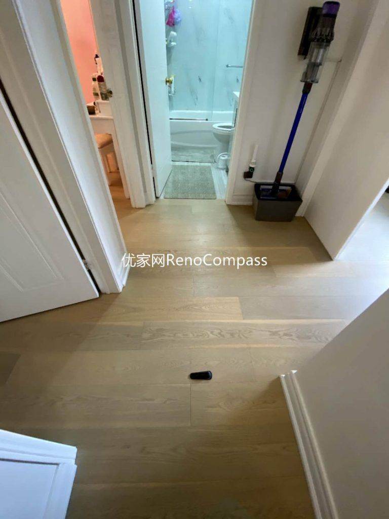This image captures a finished interior renovation in Mississauga, focusing on the hallway flooring and its seamless transition into the bathroom area. Light-toned engineered wood flooring extends throughout the corridor, creating visual continuity and a clean, modern feel, while the bathroom features durable tile flooring designed for moisture resistance and safety. Precise floor alignment, clean trim detailing, and smooth transitions between materials enhance both functionality and aesthetics. This thoughtful flooring layout supports long-term durability and everyday comfort, showcasing the careful craftsmanship of a professional Toronto renovation company.