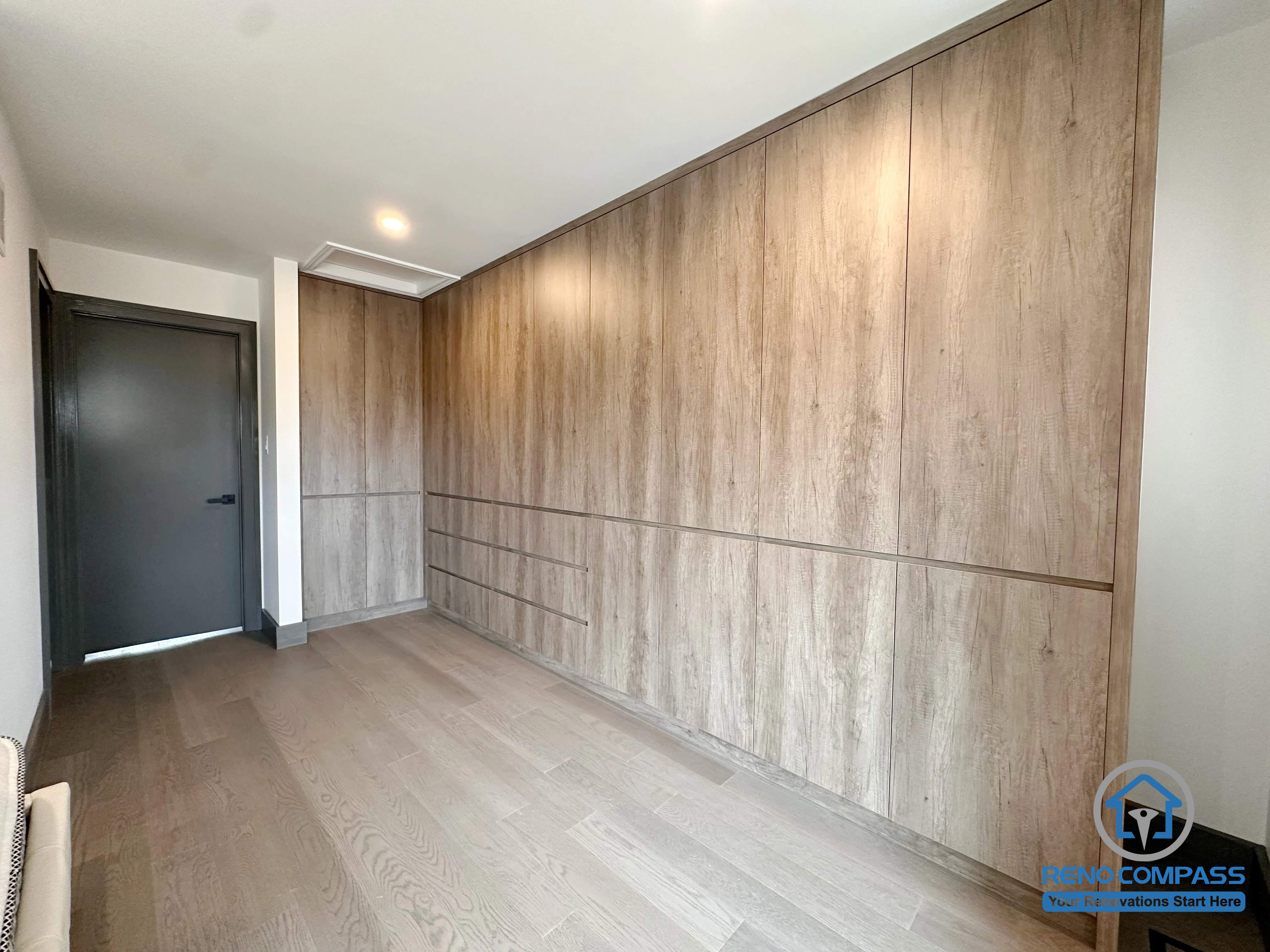 This custom built-in wardrobe system features floor-to-ceiling millwork, integrated drawers, and warm wood finishes designed to maximize storage and maintain a clean, minimalist aesthetic. The seamless cabinetry provides ample organization while complementing the home's contemporary interior design. Project completed by Reno Compass, serving Markham, Toronto, Richmond Hill, Vaughan, and the Greater Toronto Area.