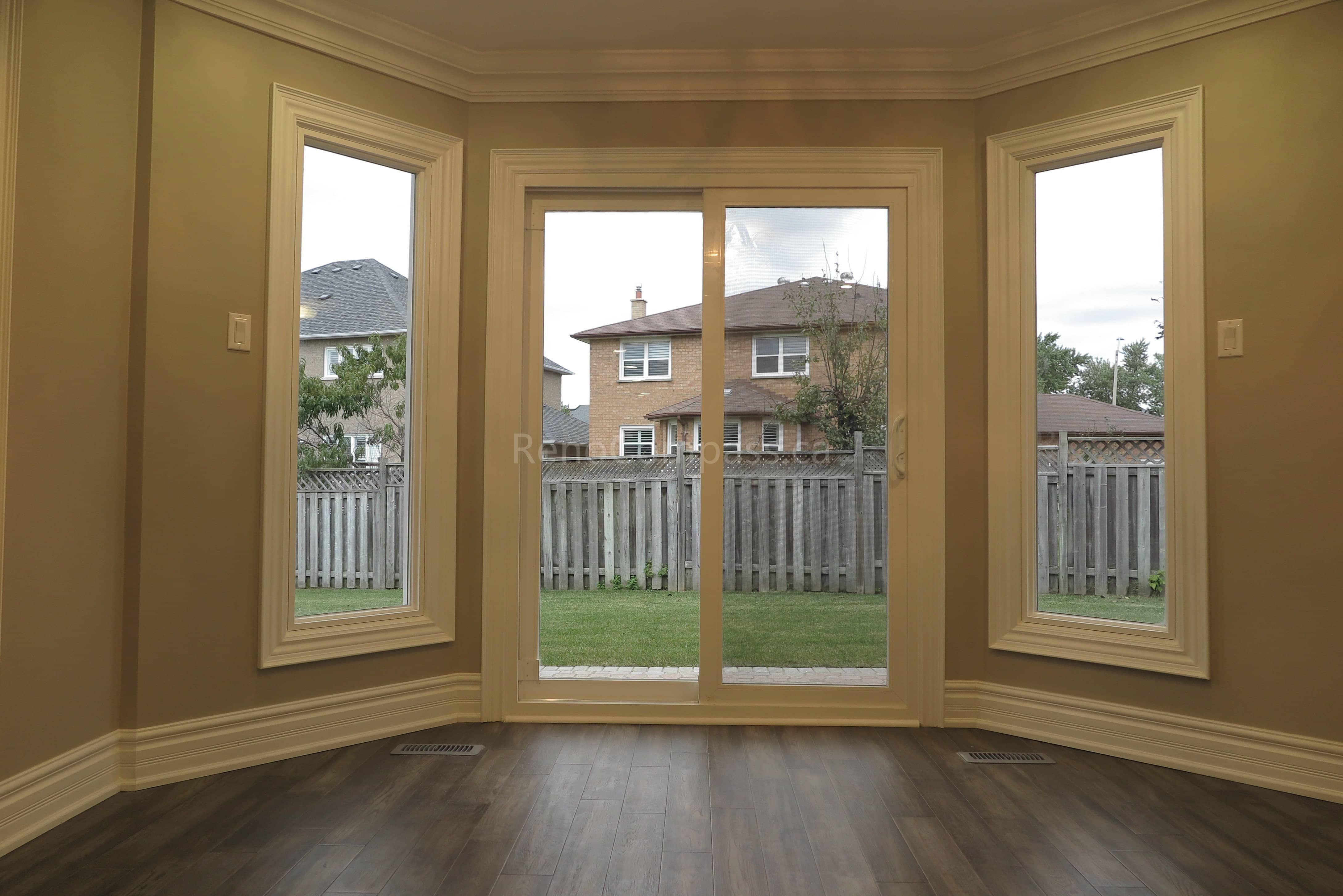This Markham interior renovation features a bright and elegant space with large custom windows and a central sliding patio door that brings in abundant natural light and backyard views. The room is finished with detailed crown molding, classic trim work, and newly installed dark hardwood flooring, creating a warm and refined atmosphere. Completed by Reno Compass, a trusted renovation contractor specializing in interior renovations and custom finishing services across Markham and the Greater Toronto Area.