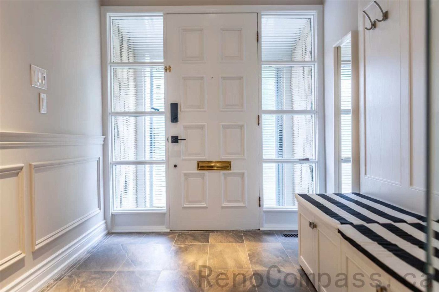 This front entry foyer is part of a North York interior renovation, designed to create a bright, organized, and welcoming first impression. The space features a solid front door with sidelights that bring in natural daylight, custom wall paneling, and durable tile flooring suited for daily use. A built-in bench with storage adds functionality for shoes and outerwear, while clean finishes and balanced proportions enhance visual clarity. The thoughtful entry layout reflects the practical design and craftsmanship found in professional Toronto interior renovation projects.