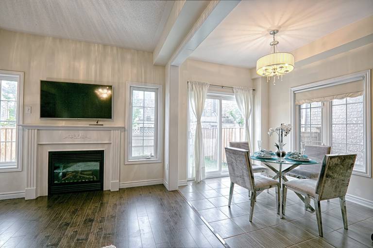 This open-concept dining and living space features a modern fireplace wall with mounted TV, elegant chandelier lighting, and large windows that bring in abundant natural light. The seamless transition between dark hardwood flooring and tiled dining space enhances visual flow and functionality. Designed with a balanced neutral palette and contemporary finishes, this interior reflects the craftsmanship of a professional Toronto renovation company specializing in stylish, functional, and modern home renovation projects.