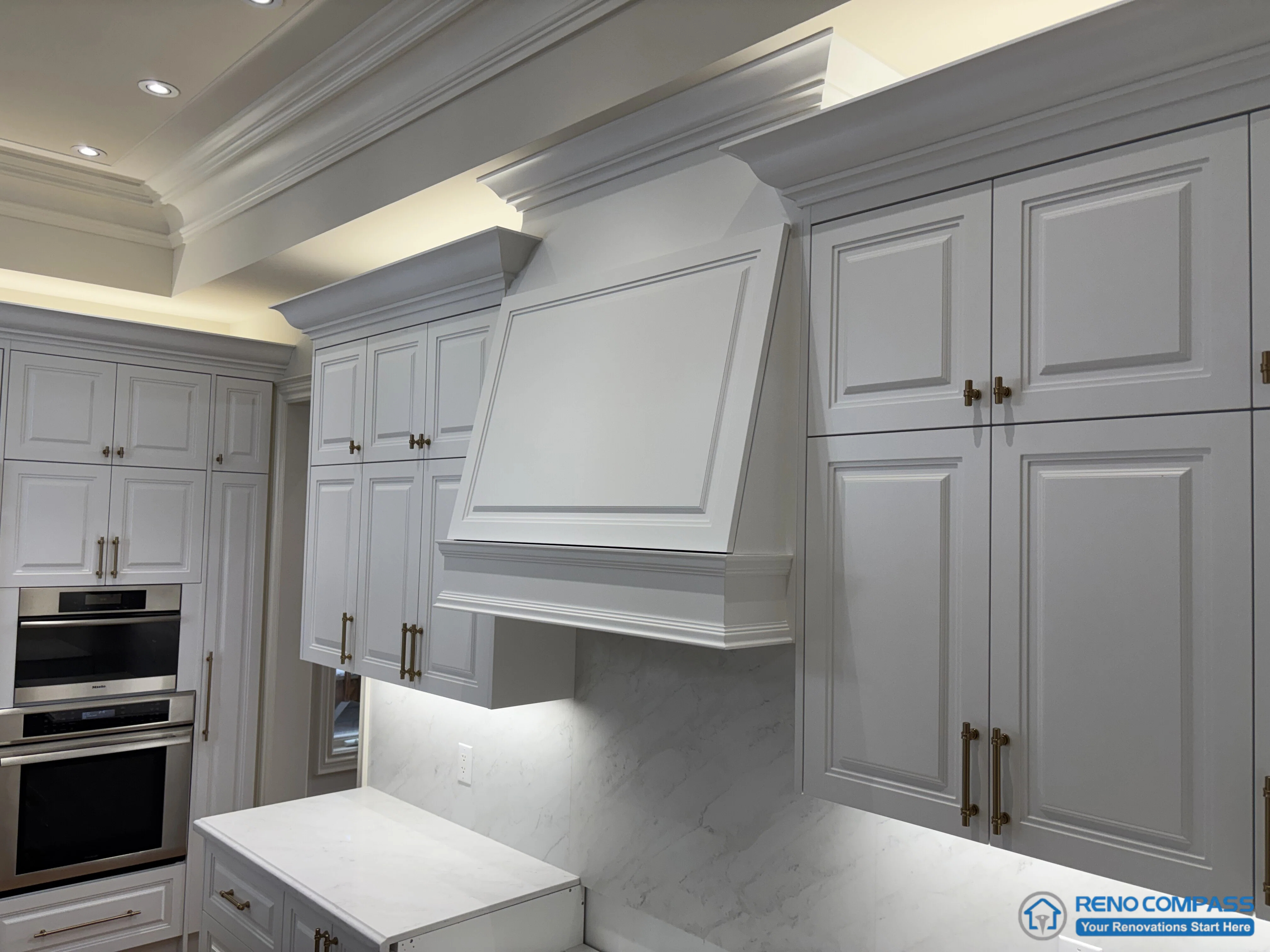 This image focuses on the main hood feature within a European-style kitchen, framed by full-height cabinetry and layered crown moulding. The hood surround is treated as an architectural centerpiece rather than a decorative add-on, with its proportions aligned to adjacent cabinet elevations. Panelled doors, classic hardware, and integrated lighting reinforce a structured and disciplined kitchen composition. The surrounding cabinetry and stone backsplash support the hood feature without competing for attention, reflecting careful coordination of scale, detailing, and craftsmanship in a high-end Richmond Hill interior renovation.