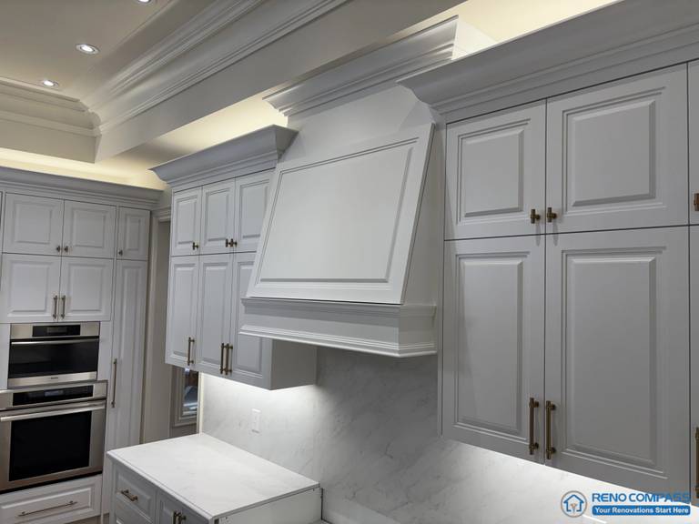 This image focuses on the main hood feature within a European-style kitchen, framed by full-height cabinetry and layered crown moulding. The hood surround is treated as an architectural centerpiece rather than a decorative add-on, with its proportions aligned to adjacent cabinet elevations. Panelled doors, classic hardware, and integrated lighting reinforce a structured and disciplined kitchen composition. The surrounding cabinetry and stone backsplash support the hood feature without competing for attention, reflecting careful coordination of scale, detailing, and craftsmanship in a high-end Richmond Hill interior renovation.