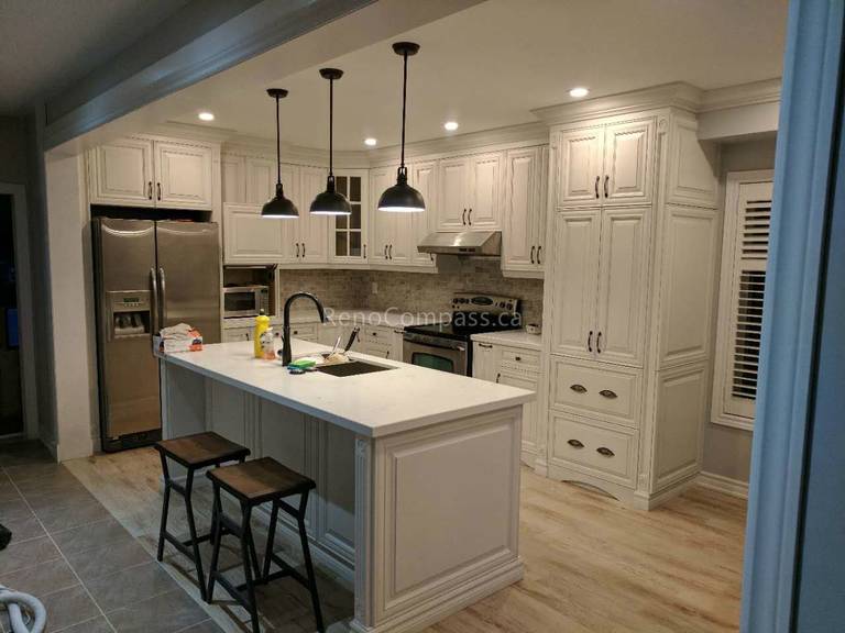 This completed Vaughan kitchen renovation by Reno Compass Inc. features custom white shaker cabinetry, a spacious quartz waterfall island with seating, and stylish black pendant lighting. The redesigned layout improves storage and functionality while stainless steel appliances and warm wood flooring create a bright, modern, and inviting kitchen space perfect for everyday family living and entertaining.
