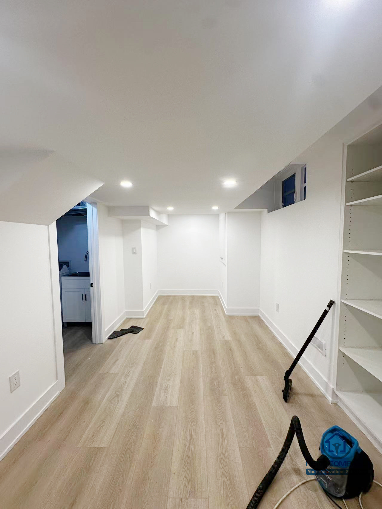 该图片展示了 Markham 室内装修项目中的地下多功能活动空间。整体采用明亮的白色墙面与浅木色地板组合，有效提升地下区域的采光感与空间通透度。嵌入式筒灯均匀分布，保证整体照明柔和且实用，适合日常活动、休闲或家庭使用。空间布局简洁利落，动线清晰，预留了充足的可塑性，可根据家庭需求灵活规划为娱乐区、健身区或储物结合空间。此类设计在保证实用性的同时，也为后期使用和功能变化提供了良好的延展性，体现了 Reno Compass 在室内翻新中对空间利用与长期居住体验的整体考量