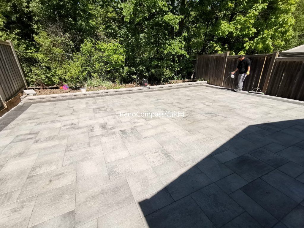 Modern Mississauga backyard patio featuring interlocking stone flooring, raised retaining wall, and landscaped garden beds, creating a functional and elegant outdoor living space.