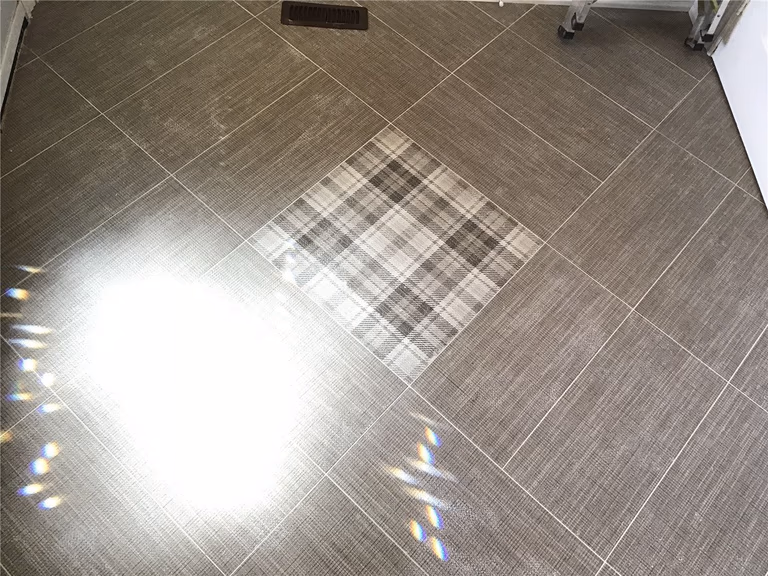 This Woodbridge interior renovation showcases durable grey porcelain floor tiles installed in a clean grid layout, enhanced by a decorative center inlay detail. The design adds visual interest while maintaining a modern and low-maintenance flooring solution, ideal for high-traffic kitchen or living areas.