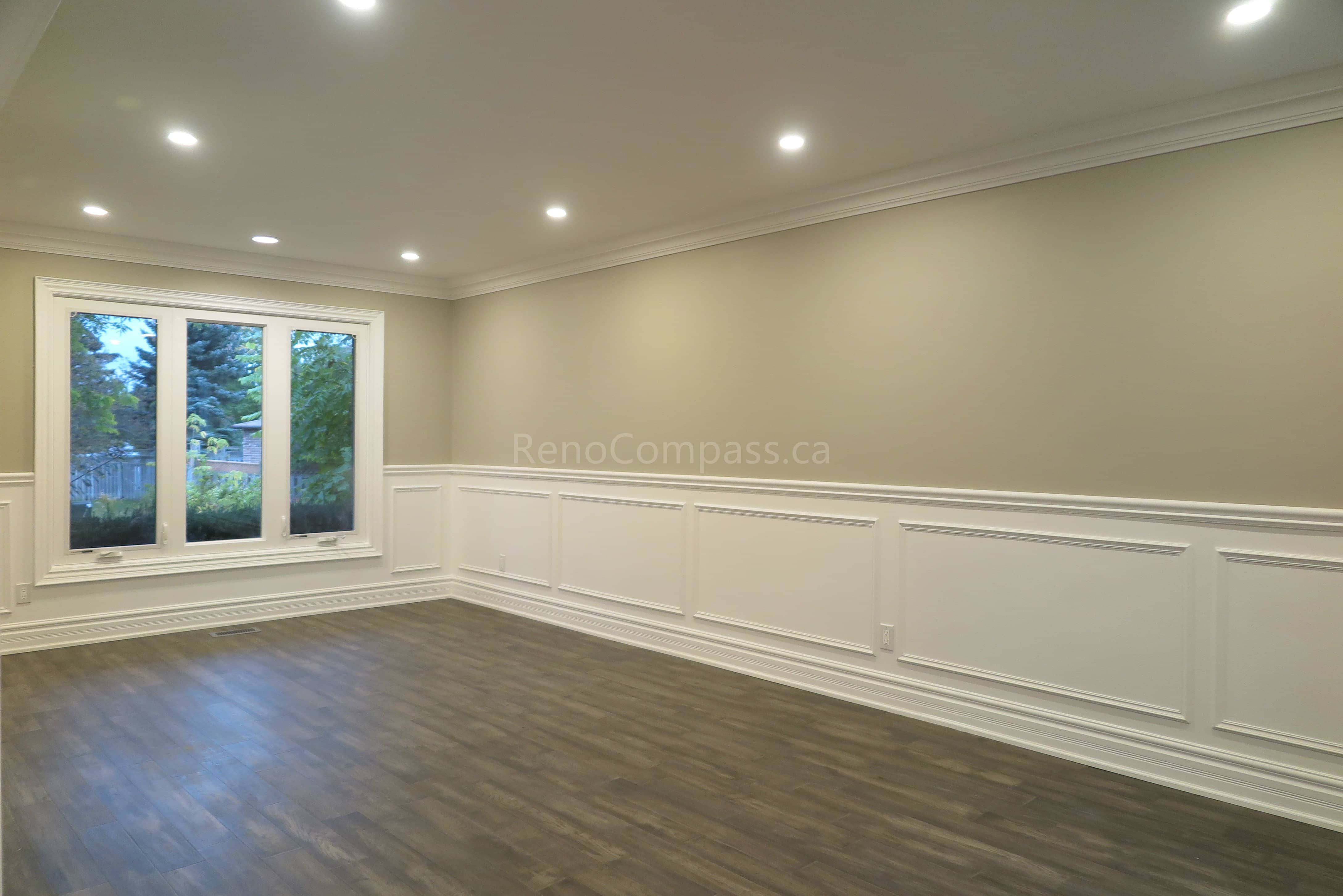 This Markham interior renovation showcases a bright and elegant living space featuring custom wall panel molding, crown molding details, and newly installed dark hardwood flooring. Recessed LED pot lights provide balanced lighting throughout the room, while large windows enhance natural light and openness. Completed by Reno Compass, a professional renovation contractor specializing in high-quality interior renovations and custom finishing services across Markham and the Greater Toronto Area.
