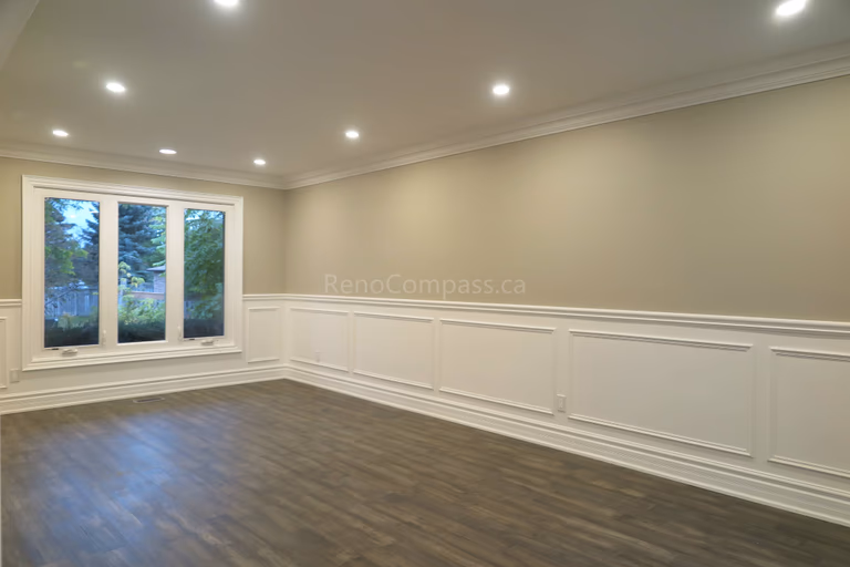 This Markham interior renovation showcases a bright and elegant living space featuring custom wall panel molding, crown molding details, and newly installed dark hardwood flooring. Recessed LED pot lights provide balanced lighting throughout the room, while large windows enhance natural light and openness. Completed by Reno Compass, a professional renovation contractor specializing in high-quality interior renovations and custom finishing services across Markham and the Greater Toronto Area.