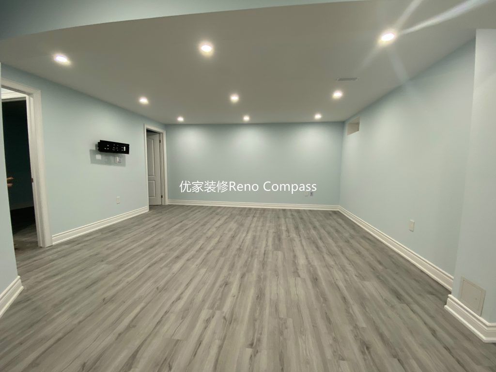 This Aurora basement renovation showcases a spacious open-concept living area completed by a professional Toronto renovation company. The upgraded basement features modern vinyl plank flooring, smooth finished ceilings with LED pot lights, and clean neutral wall tones that enhance brightness and comfort. The open layout seamlessly connects the living space to the laundry and bedroom areas, creating a functional and versatile basement ideal for family entertainment, rental use, or extended living. Contractor: Reno Compass Inc.