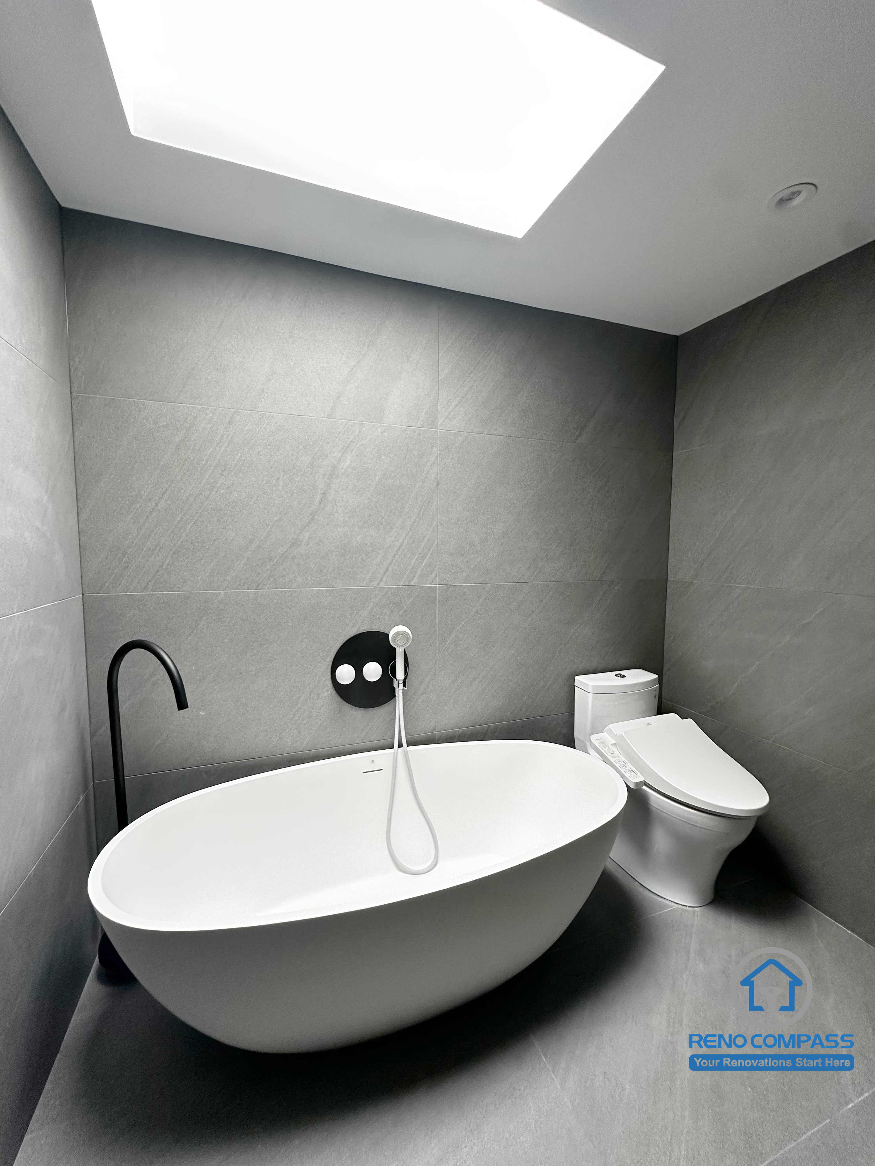 This image highlights the freestanding bathtub area in a Richmond Hill bathroom renovation. Clean architectural lines, large-format grey tiles, and a minimalist wall-mounted faucet create a calm, spa-like atmosphere. Natural light from the skylight enhances the sense of openness, while the matte black door adds contrast and depth. Designed and completed by Reno Compass, this space reflects a modern, refined bathroom renovation in the Greater Toronto Area.