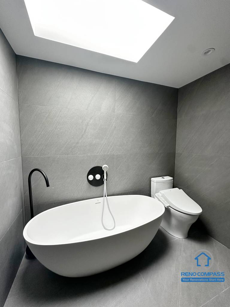 This image highlights the freestanding bathtub area in a Richmond Hill bathroom renovation. Clean architectural lines, large-format grey tiles, and a minimalist wall-mounted faucet create a calm, spa-like atmosphere. Natural light from the skylight enhances the sense of openness, while the matte black door adds contrast and depth. Designed and completed by Reno Compass, this space reflects a modern, refined bathroom renovation in the Greater Toronto Area.