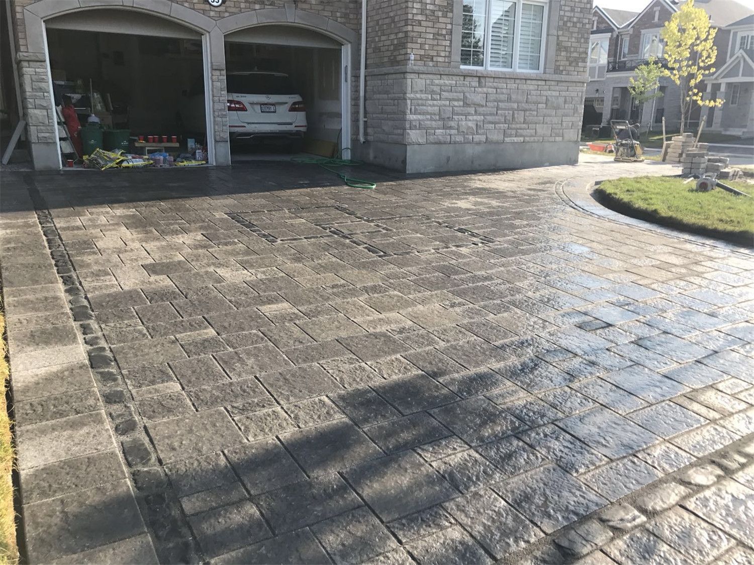 Front yard landscaping renovation in Toronto featuring a curved interlocking driveway with decorative stone borders. The design enhances curb appeal while creating a durable and visually appealing driveway layout that complements the home’s architecture.