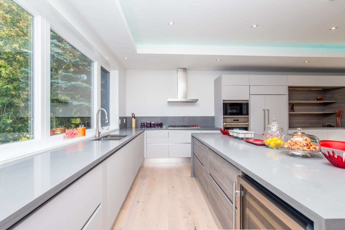 High-end modern kitchen renovation in a 5000 sqft Toronto custom home featuring sleek grey cabinetry, expansive quartz countertops, a large central island with built-in wine fridge, and full-height storage units. The bright open layout is enhanced by large windows, recessed lighting, and clean contemporary finishes designed for both everyday living and entertaining. Completed by Reno Compass Inc., a trusted Toronto renovation company specializing in luxury kitchen renovations and full home interior remodeling.