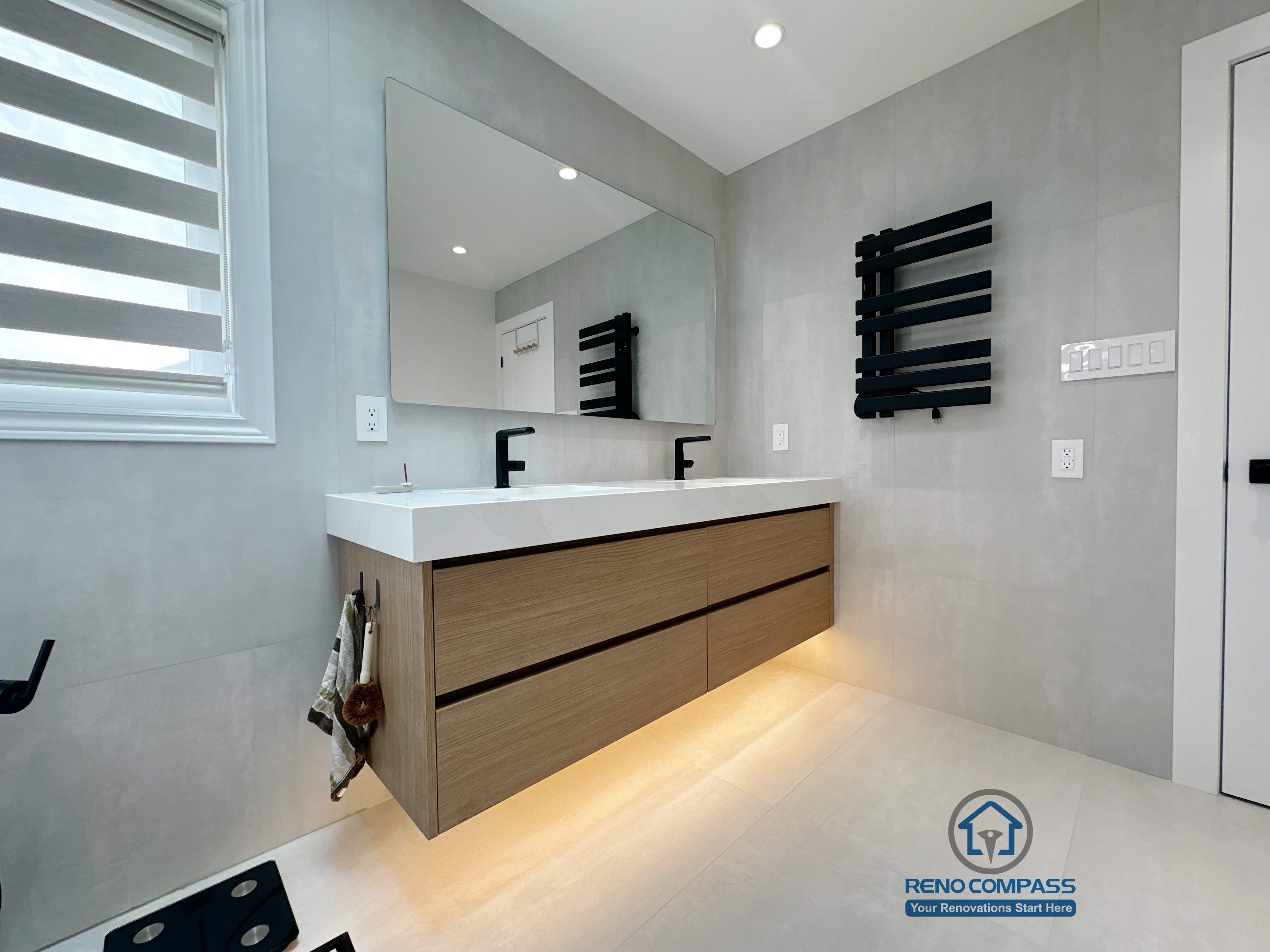 A minimalist bathroom renovation by Reno Compass in Markham, Toronto.
This space features a floating double-sink vanity with warm under-cabinet lighting, clean wall finishes, and a balanced layout that enhances daily functionality and visual clarity.