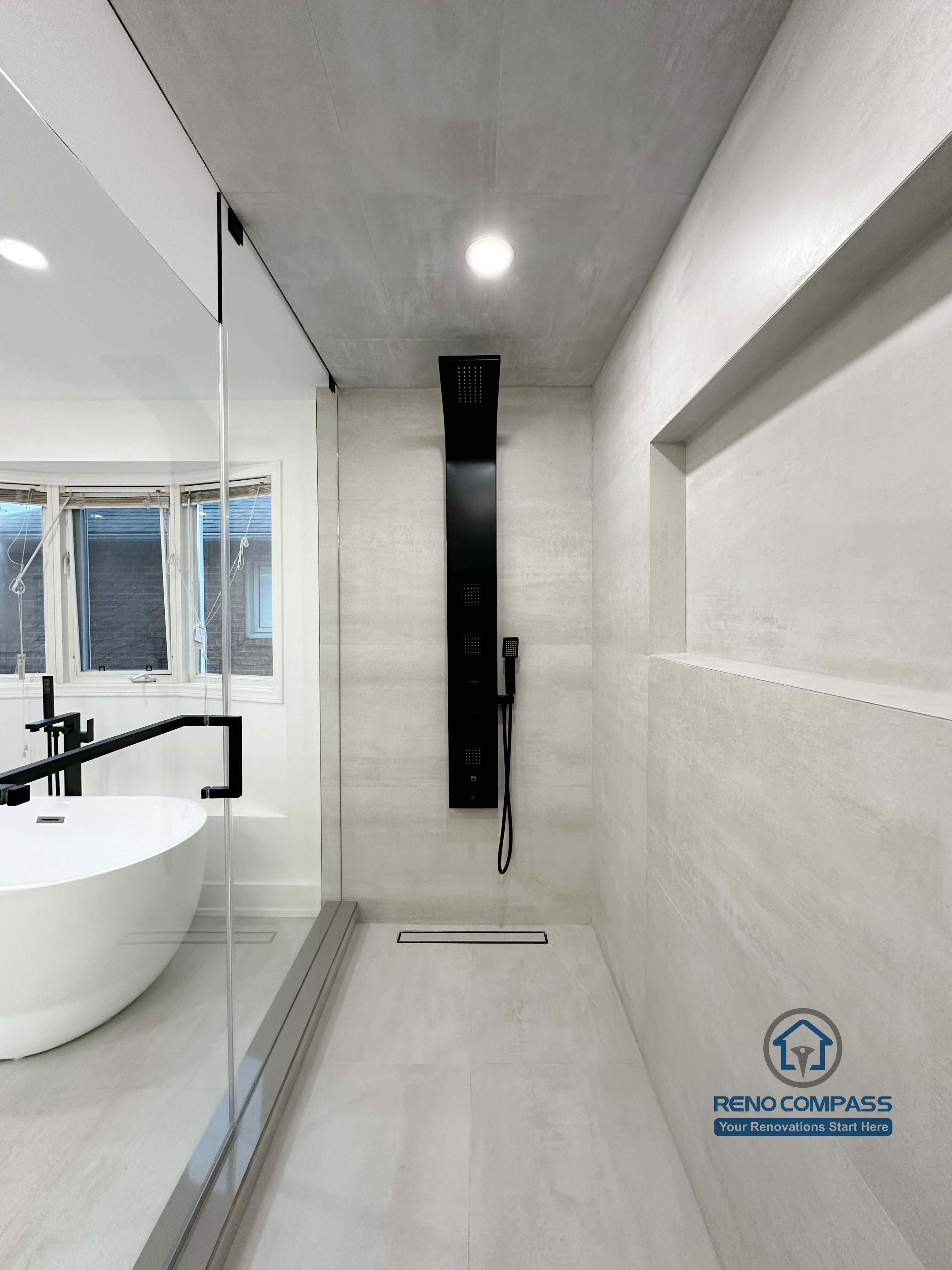 Oakville bathroom renovation showcasing a modern black shower panel, linear floor drain, large-format tile walls, and frameless glass enclosure, completed by a professional Toronto renovation company.