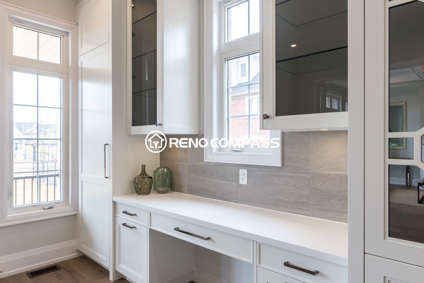 Elegant kitchen renovation in Newmarket featuring custom white cabinetry, built-in storage, and a bright window-side countertop workspace. The design combines modern finishes, glass cabinet doors, and clean lines to create a functional and stylish kitchen environment.