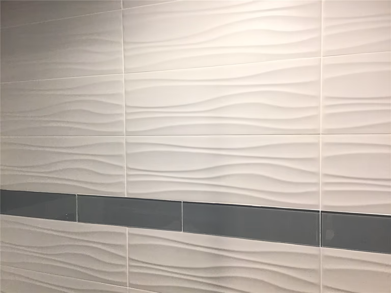 Close-up of modern 3D wave-pattern wall tiles installed in this Richmond Hill basement renovation project. The textured beige tiles are enhanced with a sleek horizontal accent strip, adding depth, visual movement, and a contemporary finish to the basement bathroom design.