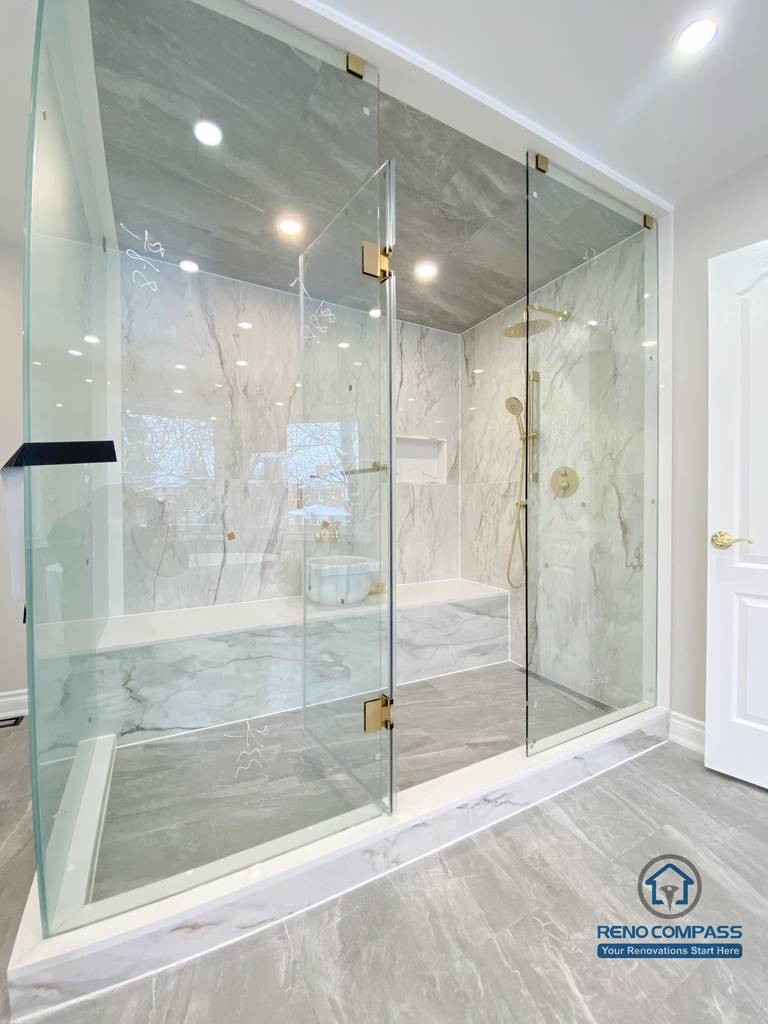 This Richmond Hill bathroom renovation showcases a bright and elegant design featuring a frameless glass shower enclosure, built-in bathtub, marble-style wall tiles, and gold-finish fixtures. The custom white vanity with integrated lighting mirror and large-format floor tiles enhance both functionality and visual openness. This project reflects high-quality craftsmanship and thoughtful layout planning for a modern bathroom renovation in Richmond Hill.