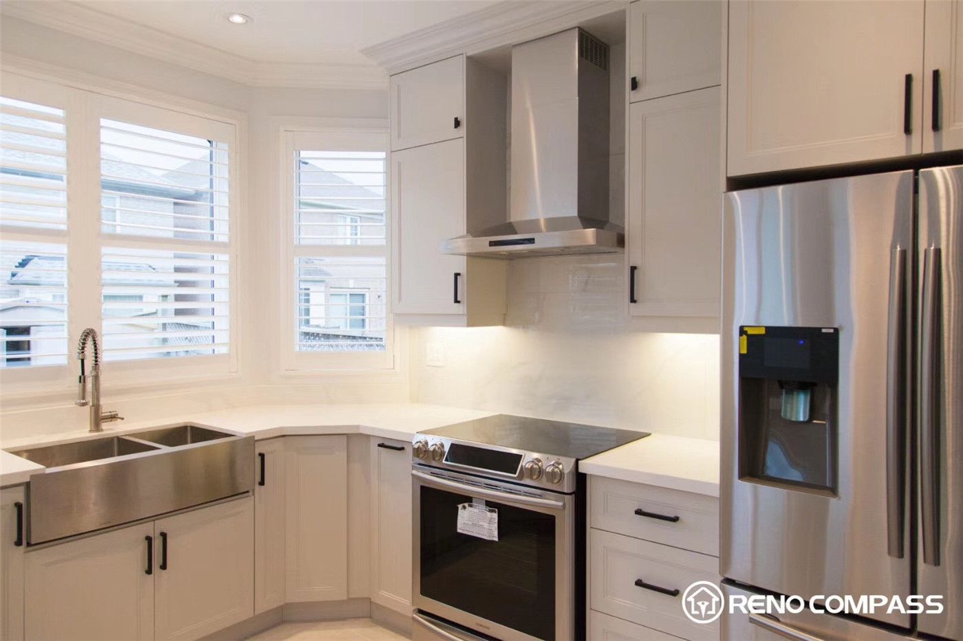 This Markham kitchen renovation features a bright and elegant layout with white shaker cabinets, quartz countertops, and modern stainless steel appliances. The corner sink placement maximizes window views and natural light, while the clean backsplash and sleek range hood create a fresh and functional cooking space.
