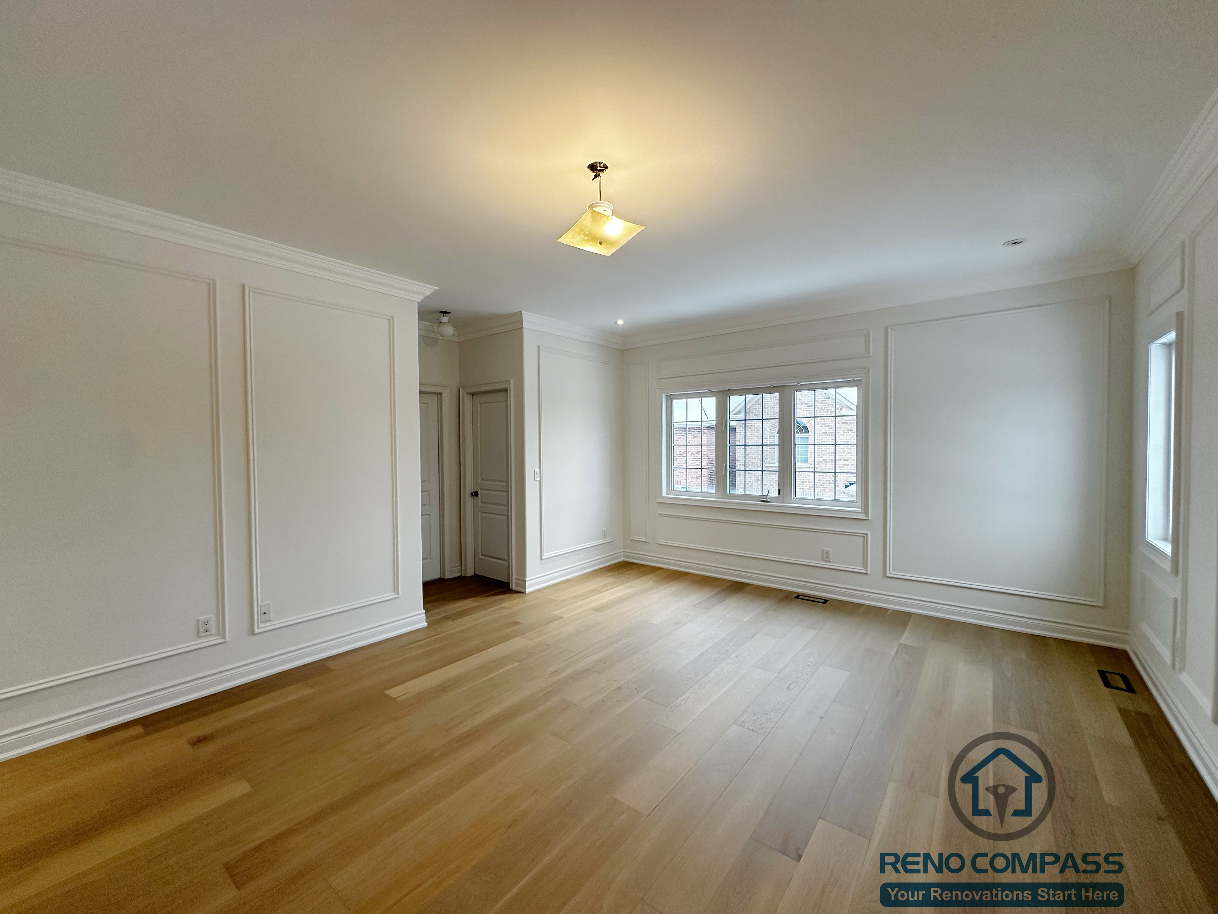Bright and spacious bedroom completed as part of a Vaughan interior renovation, featuring custom wall panel detailing, crown moulding, wide-plank hardwood flooring, and large windows that enhance natural light. The clean and timeless design reflects refined craftsmanship by a professional Toronto renovation company.