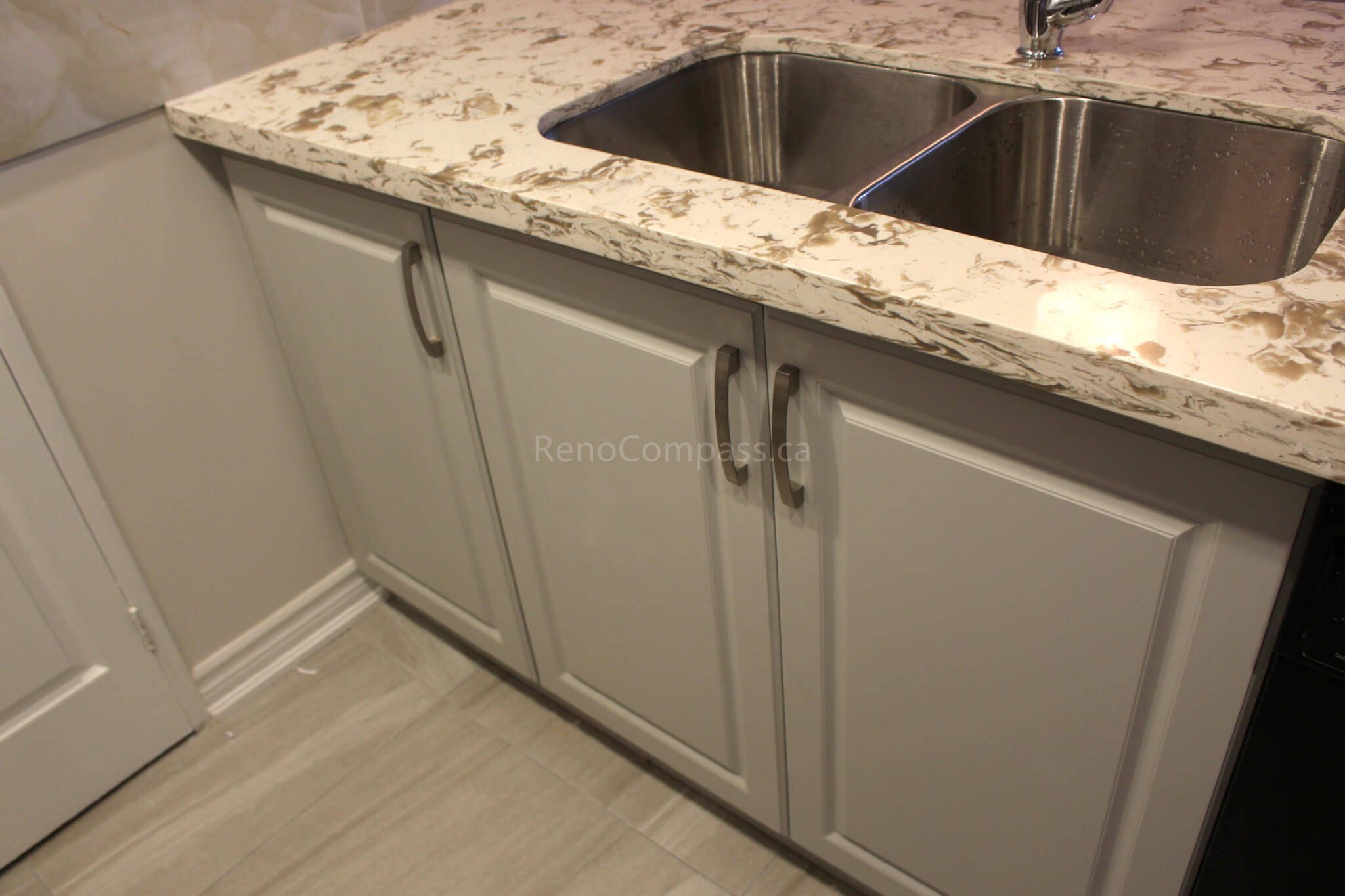 A beautifully renovated Mississauga kitchen featuring elegant white cabinetry, a polished quartz countertop, and a sleek double stainless steel sink. Part of a full interior renovation project focusing on modern finishes and functionality.