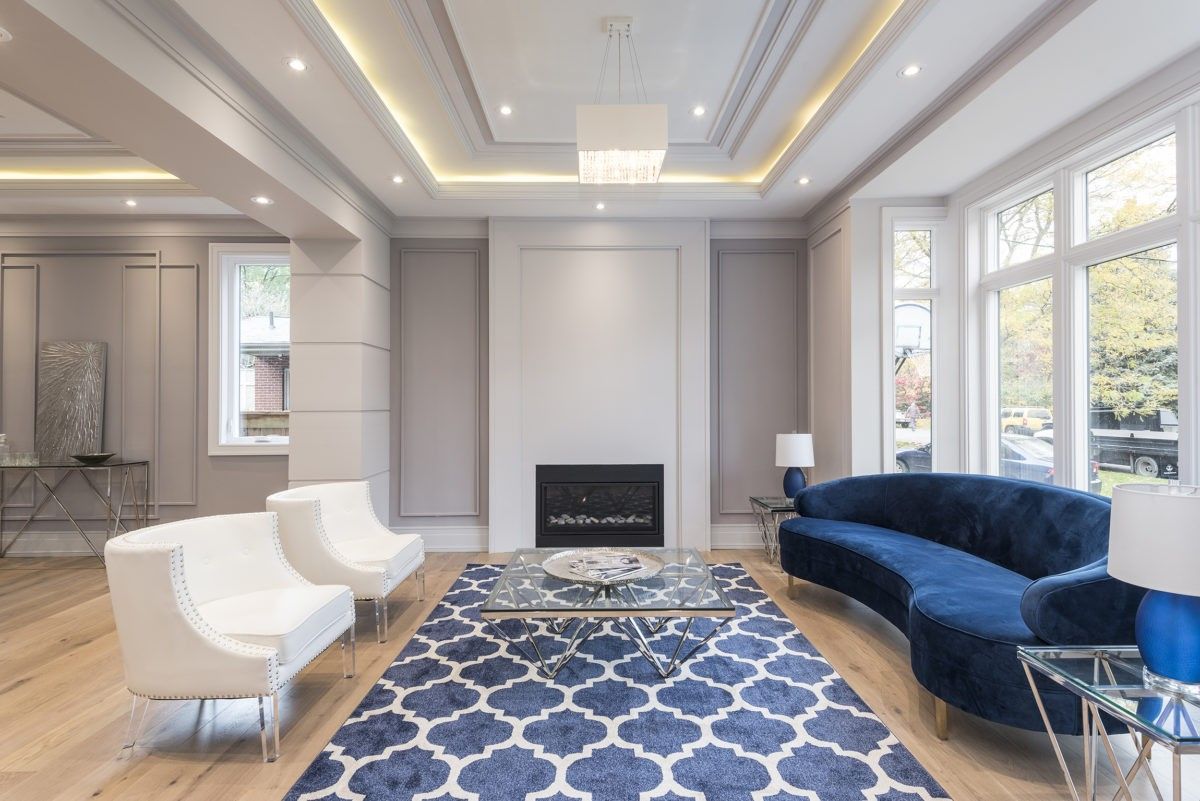 This Newmarket interior renovation features a bright and elegant living room designed by a professional Toronto renovation company. The space includes custom wall panel molding, a modern built-in fireplace, wide plank hardwood flooring, and large windows that bring in natural light. A coffered ceiling with recessed LED lighting enhances the luxury atmosphere, while contemporary furniture and a statement rug complete the sophisticated design. This renovation transforms the living area into a stylish and comfortable space ideal for modern family living in Newmarket and the GTA.