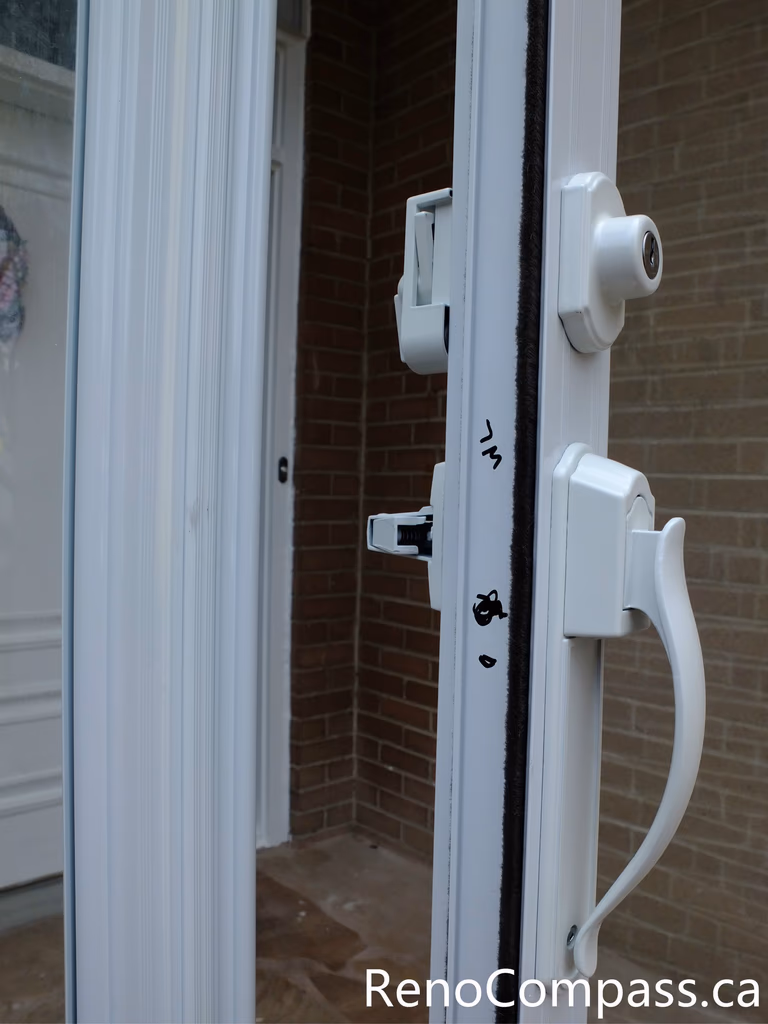 This close-up image shows the handle and lock detail of a newly installed glass storm door at a North York residential entrance. The durable white handle and secure locking system provide convenient access while improving safety and weather protection. The storm door enclosure helps shield the main entrance from wind, snow, and rain, while the clear glass panels allow natural light to enter the foyer. Installed by a professional Toronto renovation team, this entrance upgrade enhances both security and the overall appearance of the home.