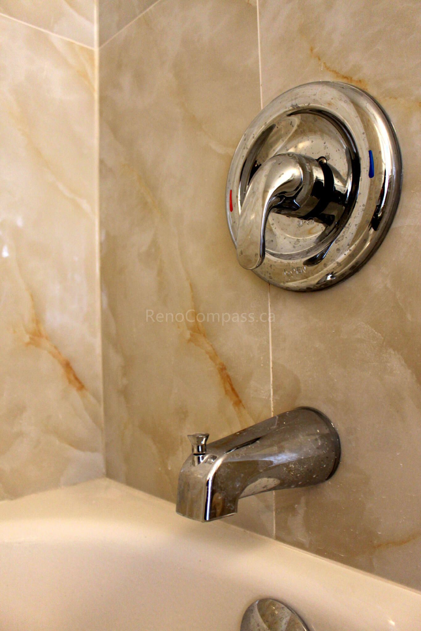A close-up of a modern bathtub and chrome faucet set against elegant marble-style wall tiles. This Mississauga bathroom renovation combines durability with a luxurious, spa-like aesthetic — completed by RenoCompass for a stylish interior upgrade.
