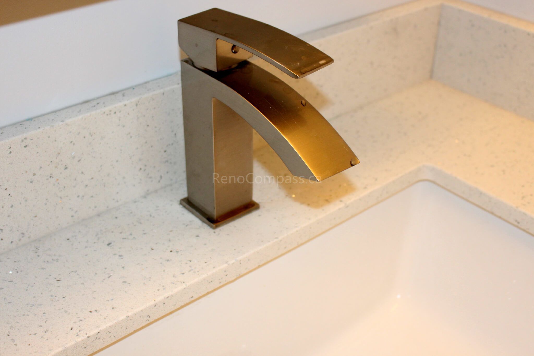 Close-up detail of a modern gold waterfall faucet installed on a white quartz countertop during a Mississauga interior renovation project. This elegant bathroom upgrade combines contemporary fixtures with durable materials for a clean and luxurious finish. Completed by Reno Compass, a professional Toronto renovation company, the project highlights quality craftsmanship and stylish bathroom design for GTA homes.