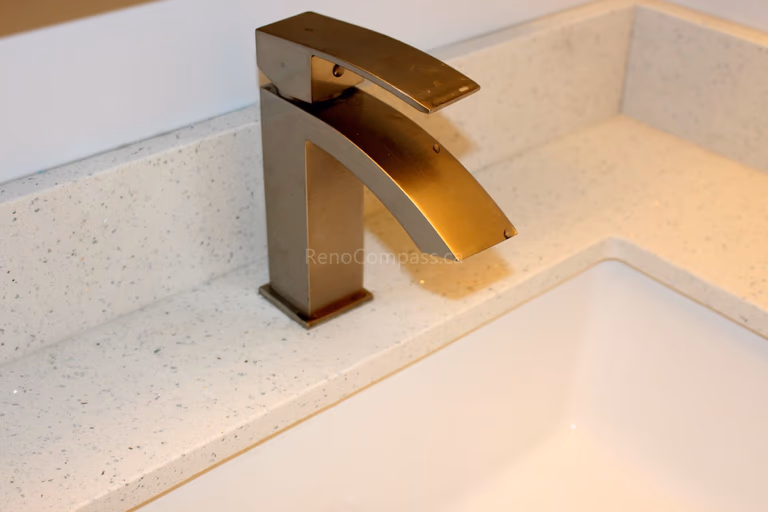 Close-up detail of a modern gold waterfall faucet installed on a white quartz countertop during a Mississauga interior renovation project. This elegant bathroom upgrade combines contemporary fixtures with durable materials for a clean and luxurious finish. Completed by Reno Compass, a professional Toronto renovation company, the project highlights quality craftsmanship and stylish bathroom design for GTA homes.