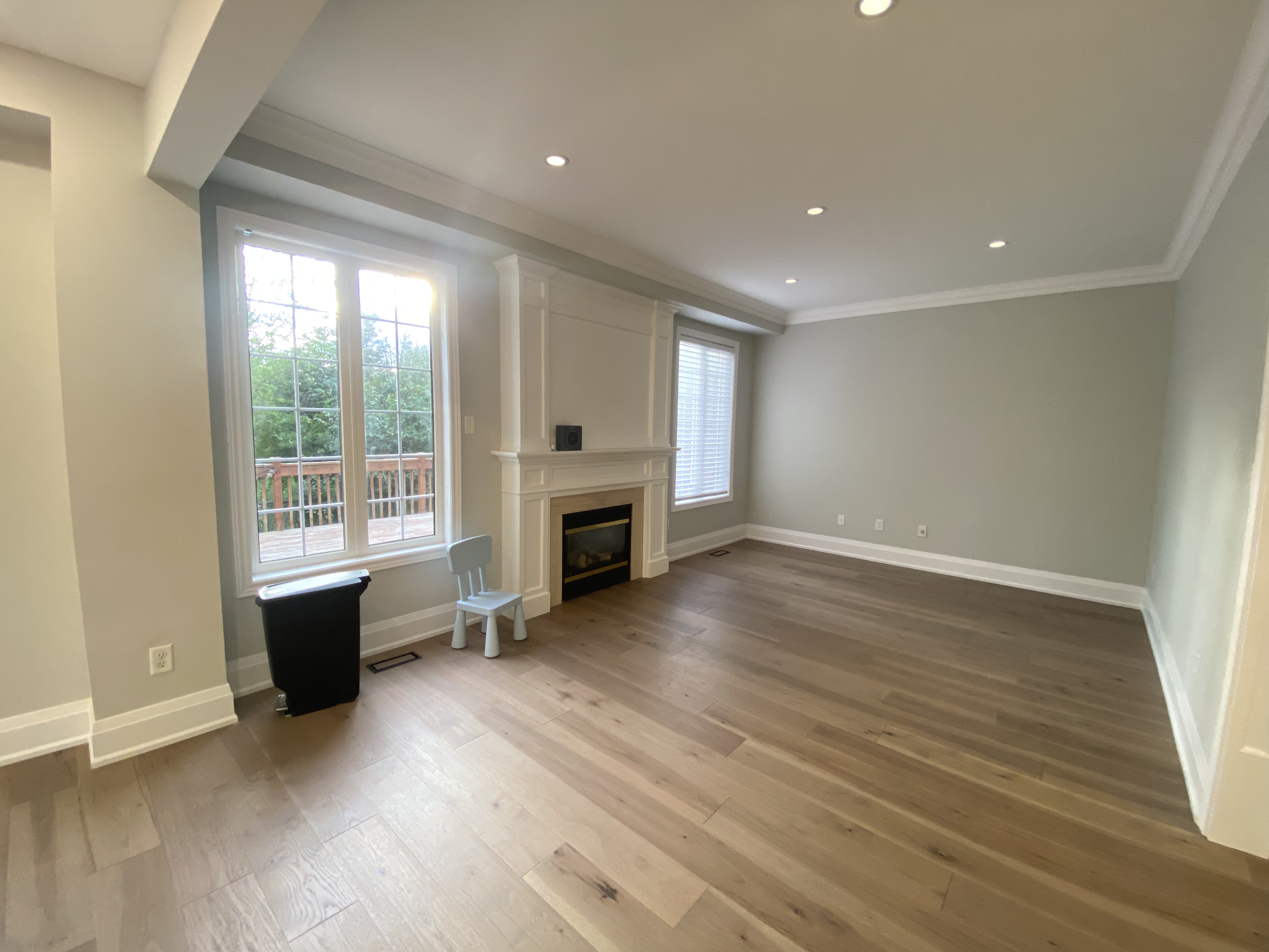 A bright and spacious living room completed as part of a Richmond Hill interior renovation. This space features wide-plank hardwood flooring, recessed ceiling lighting, large windows for natural light, and a clean-lined fireplace focal wall.