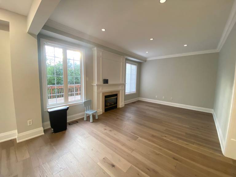 A bright and spacious living room completed as part of a Richmond Hill interior renovation. This space features wide-plank hardwood flooring, recessed ceiling lighting, large windows for natural light, and a clean-lined fireplace focal wall.